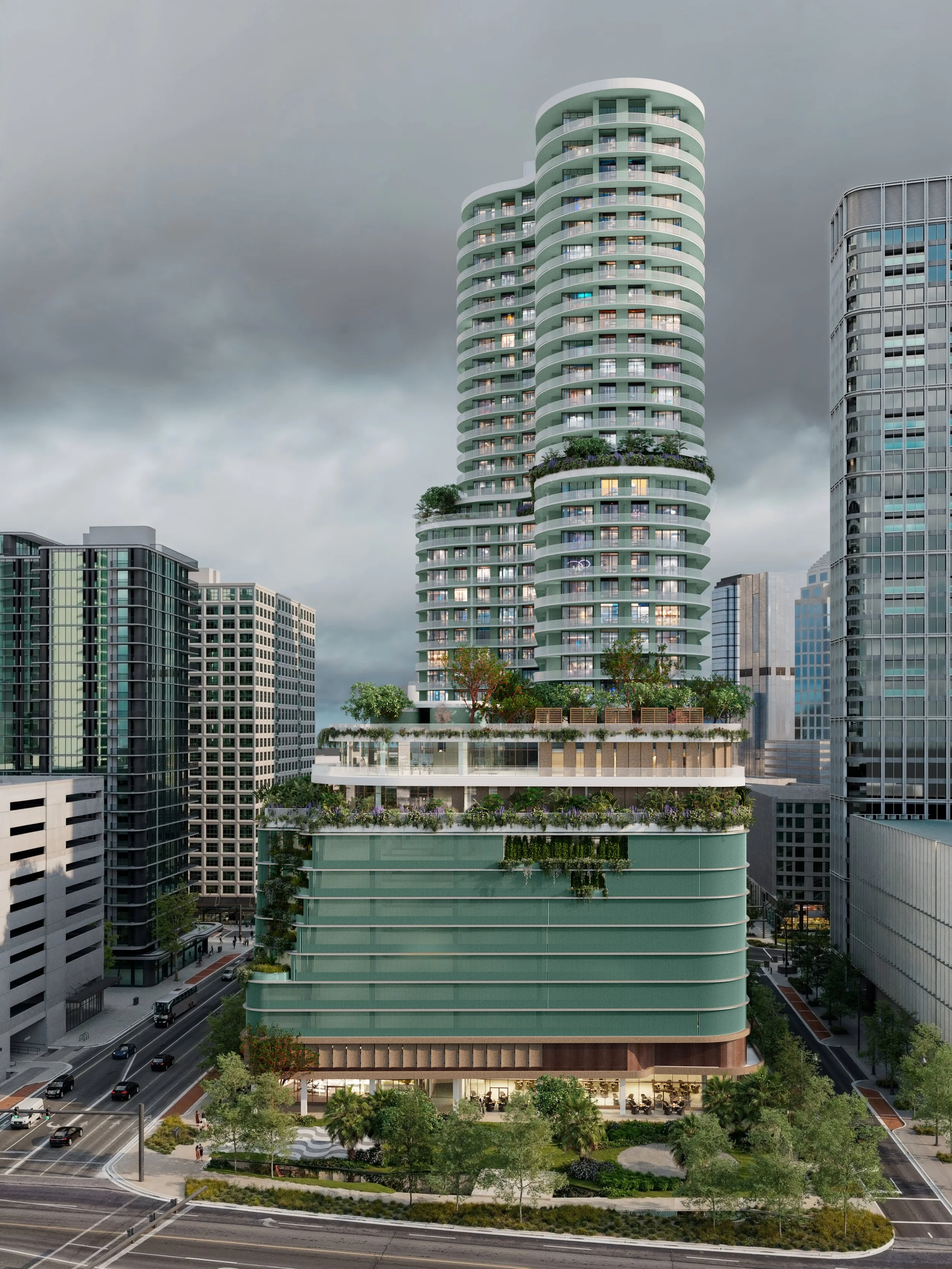 Modern high-rise building with multiple terraced green spaces and trees, located in a cityscape with other skyscrapers and parking lots nearby, under a cloudy sky.