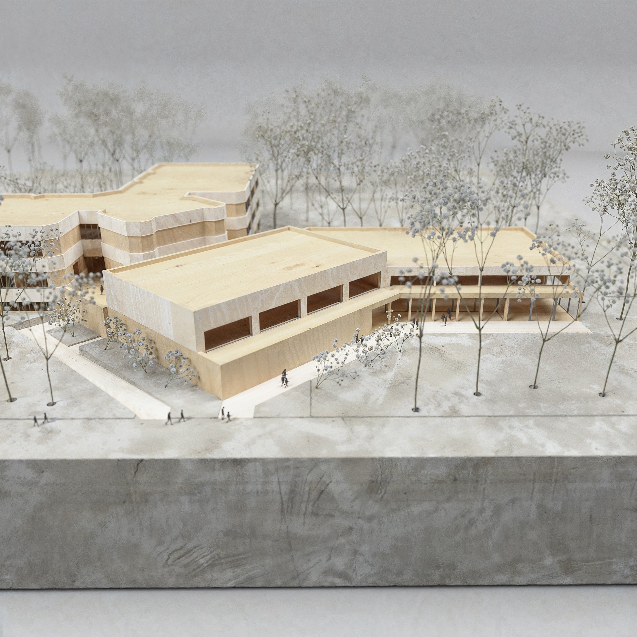 Architectural model of a modern building with multiple levels, surrounded by trees and small human figures for scale.