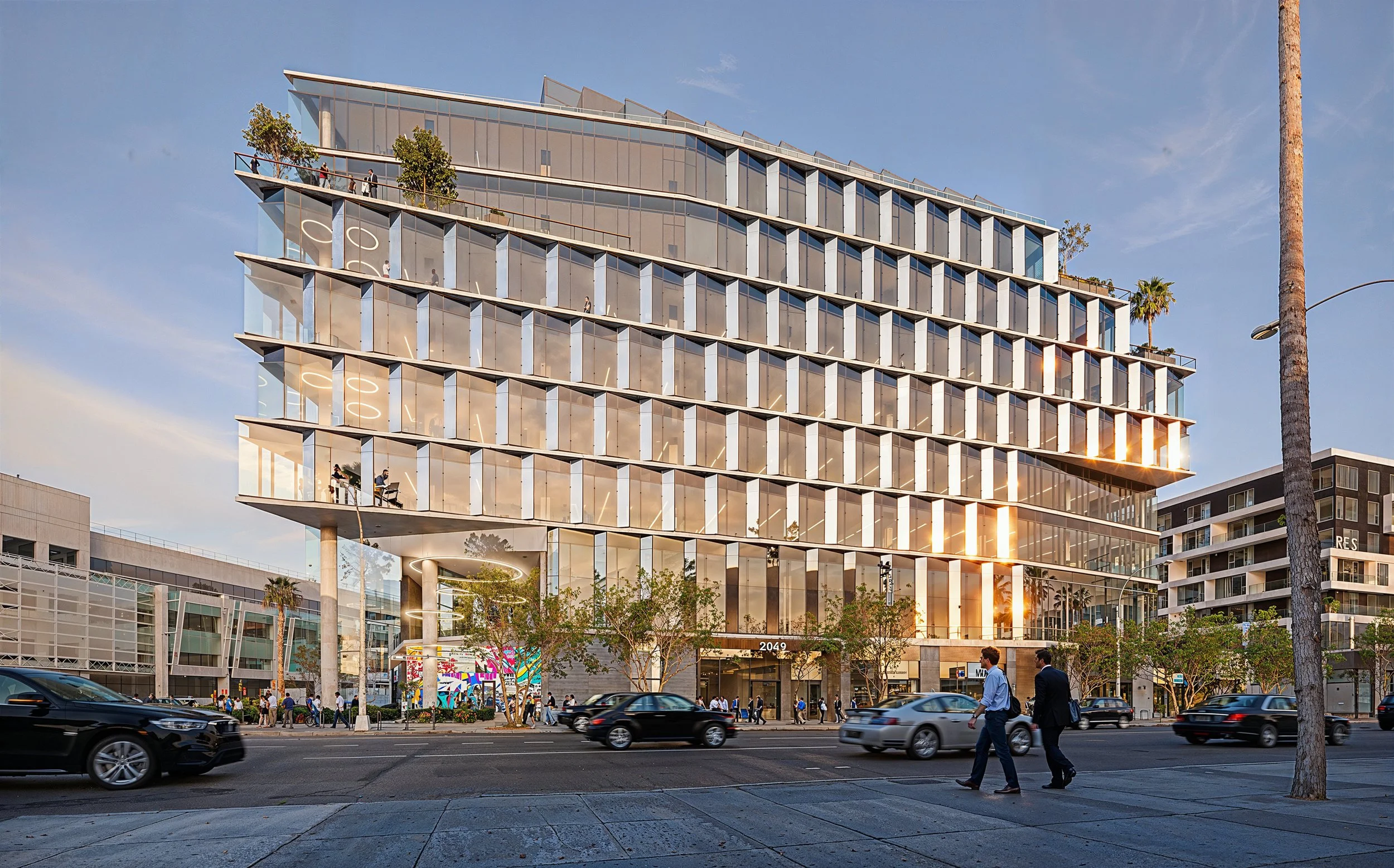 Modern multi-story glass office building reflecting the sunset in downtown Los Angeles with pedestrians and cars on the street.
