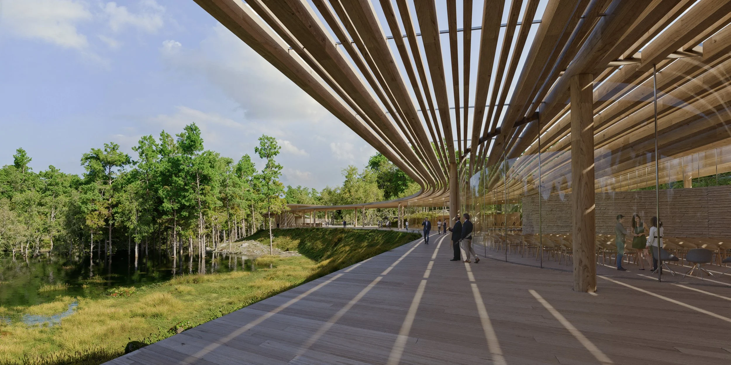 Modern building with wooden slatted roof, glass walls, and people walking and talking outside on a curved wooden deck, surrounded by lush green trees and a body of water.
