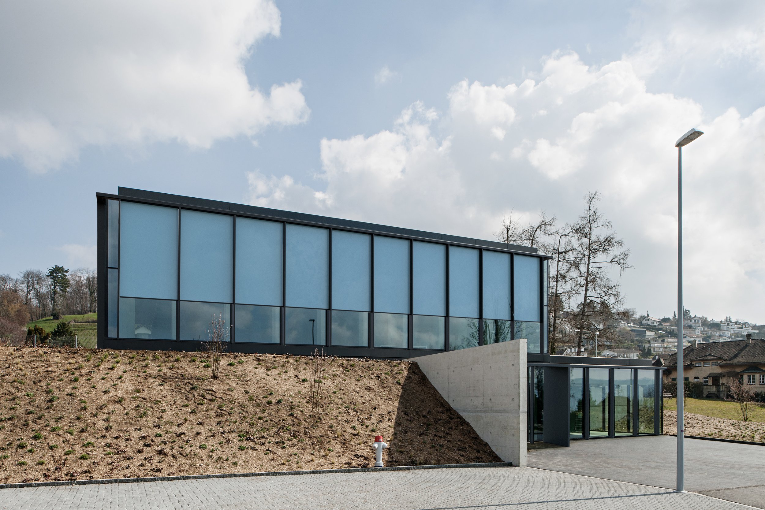 Modern building with large glass windows on a slight hillside against a partly cloudy sky.
