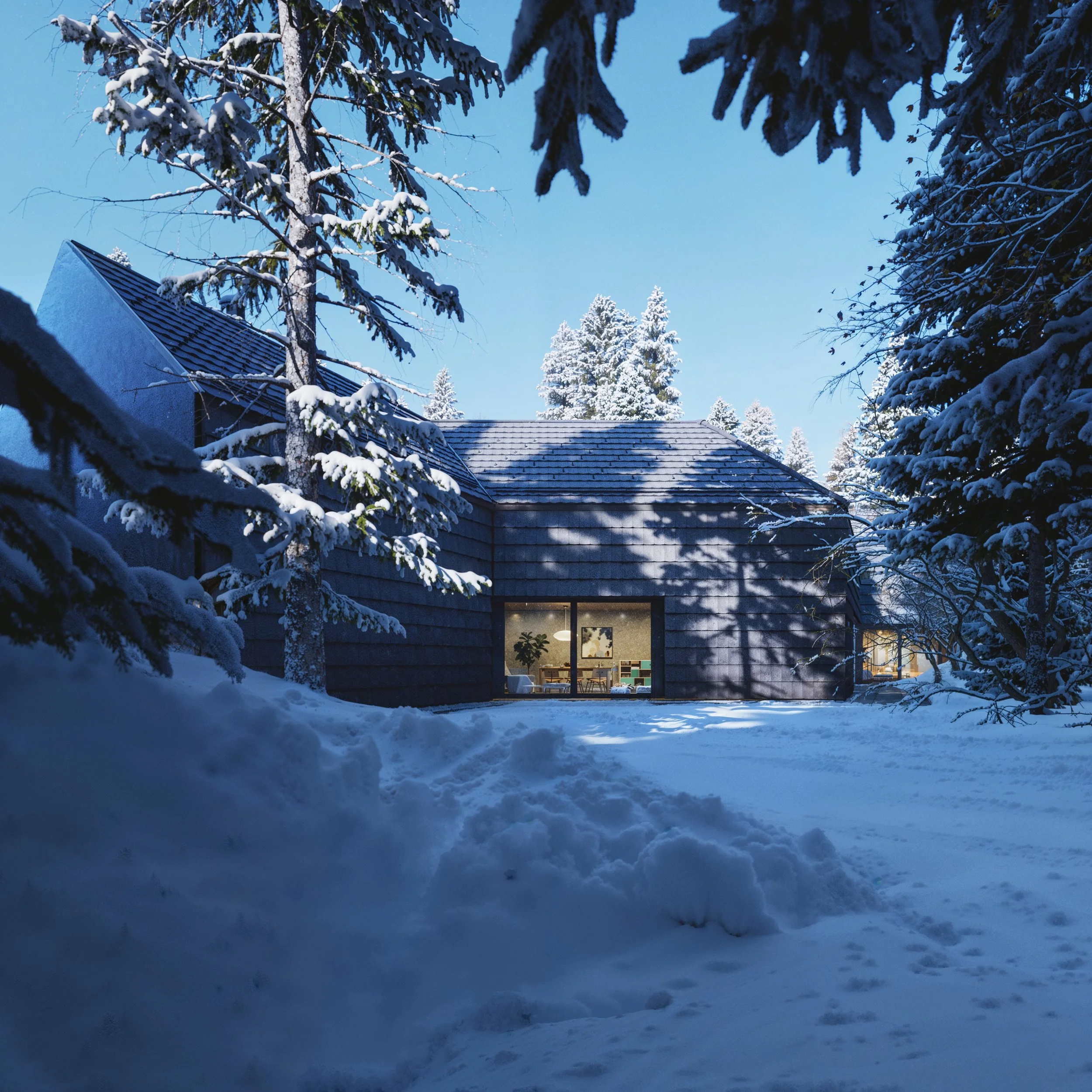 A snow-covered modern house viewed through snow-laden trees, with lit interior visible through large windows, under a clear blue sky.