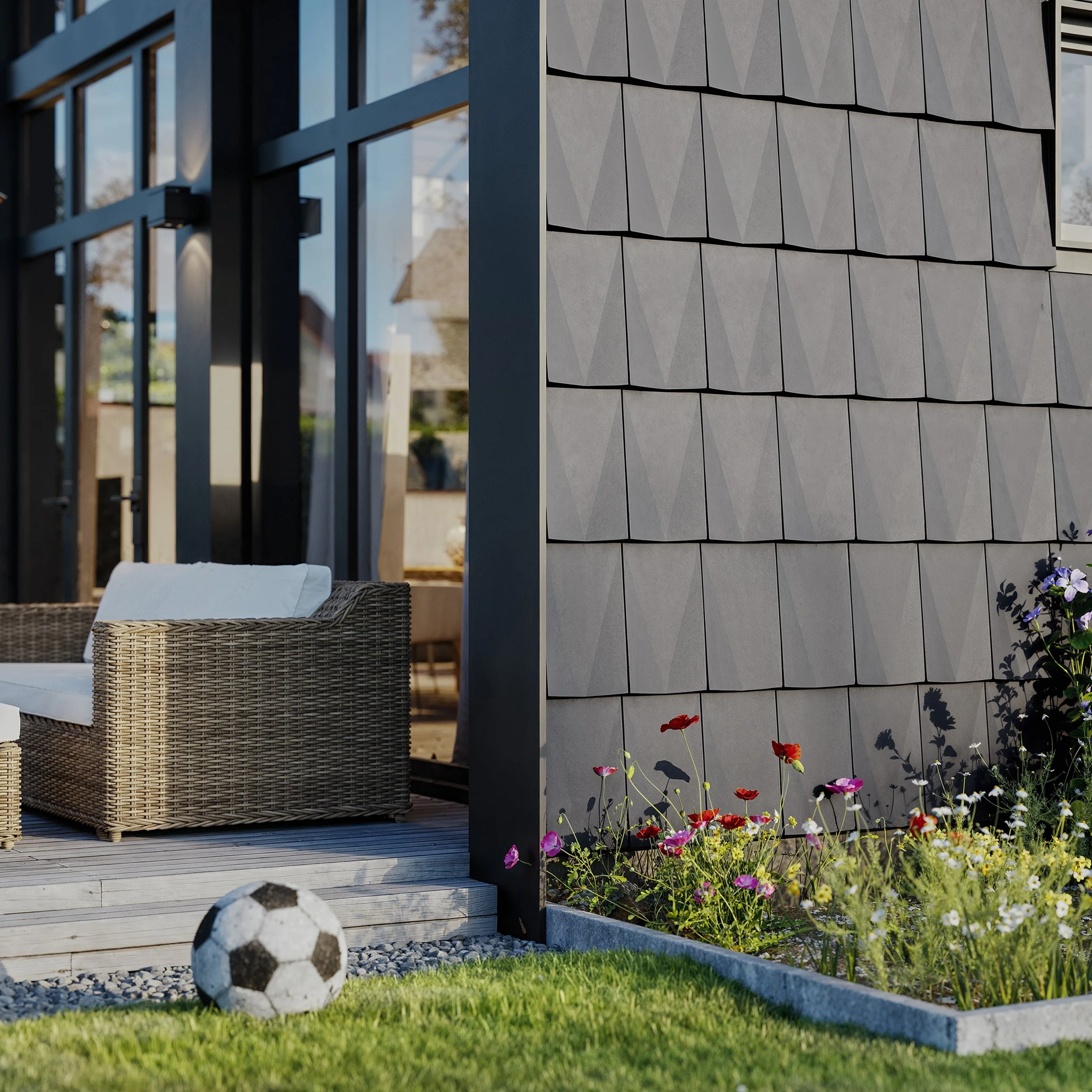 A soccer ball on a grassy lawn near a garden bed with colorful flowers in front of a modern house with large glass windows and a tiled exterior wall.