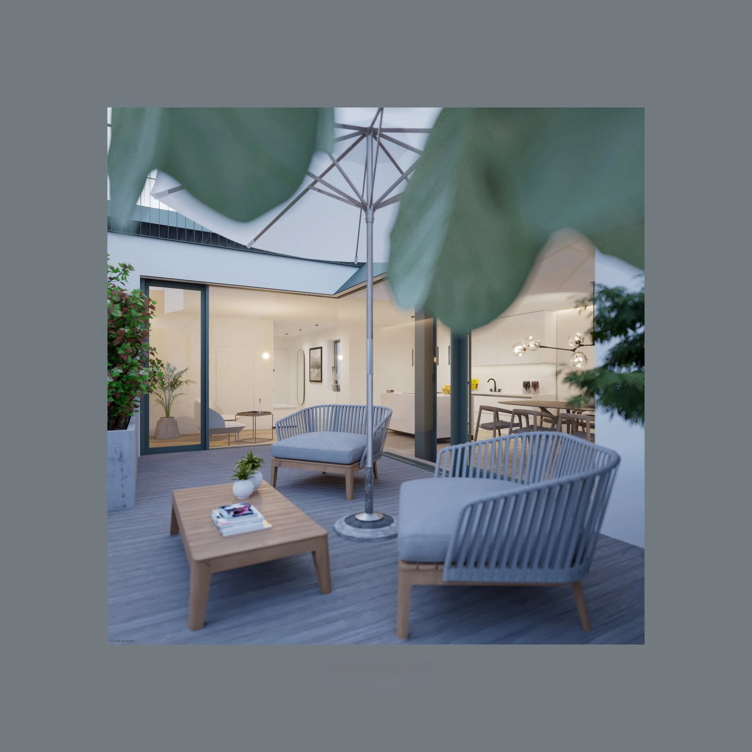 A modern outdoor patio with wooden furniture, chairs with cushions, a coffee table with magazines, large green leaves overhead, and a view into a bright indoor living space through large glass doors.