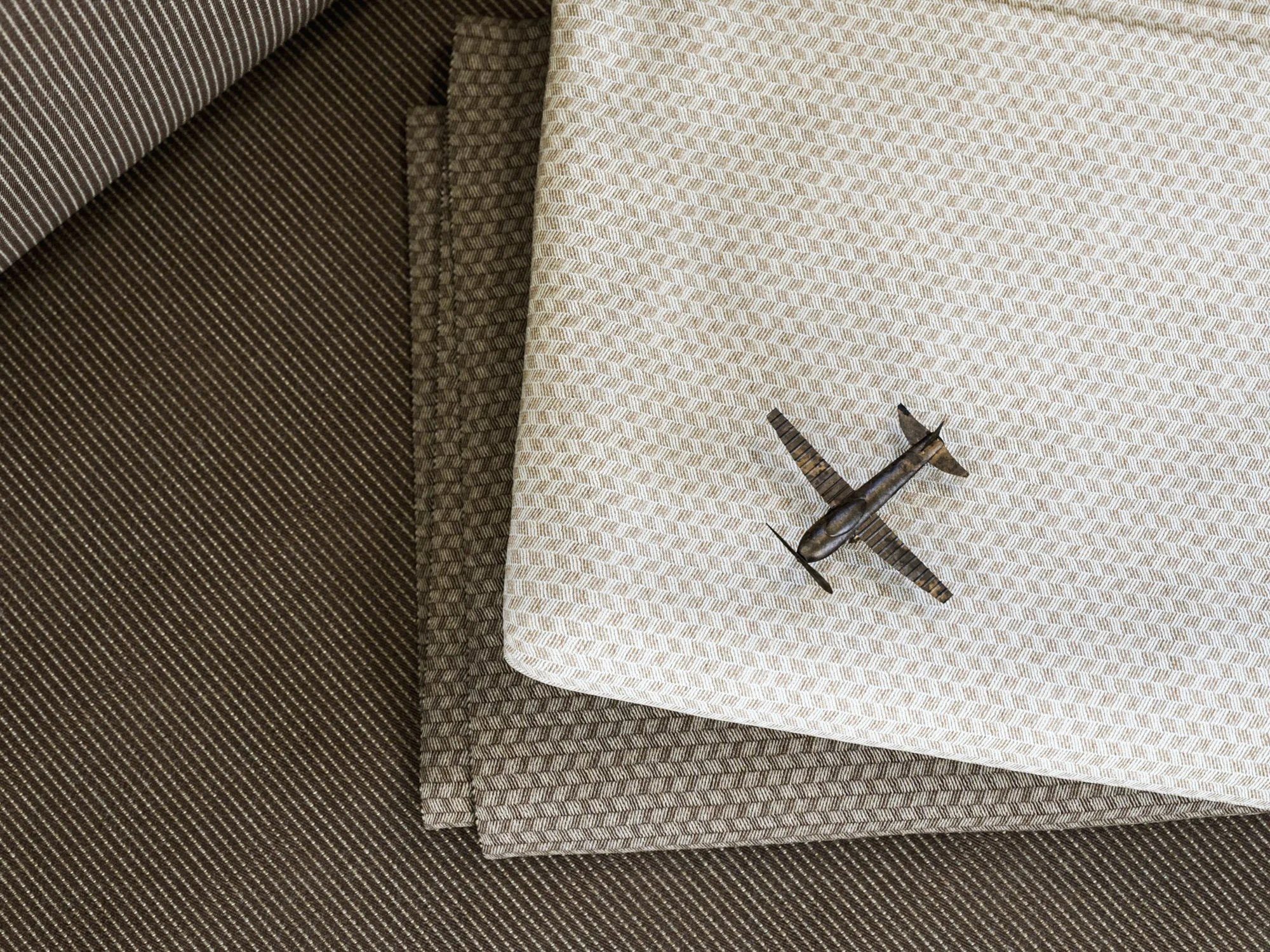 Three fabrics with striped patterns layered on top of each other, with a small model airplane placed on the top fabric.