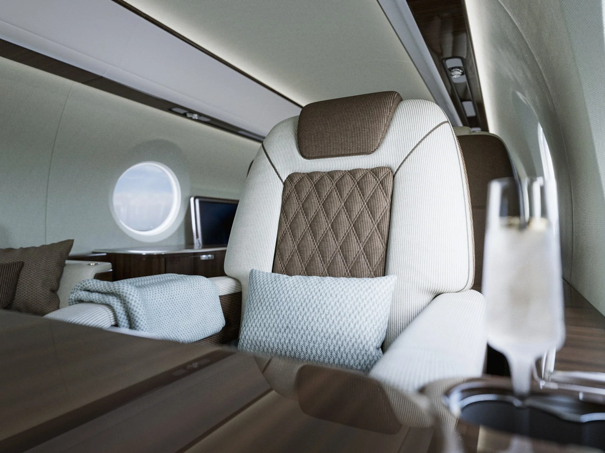 Empty first class airplane seat with brown and white upholstery, a pillow, and a window in the background.
