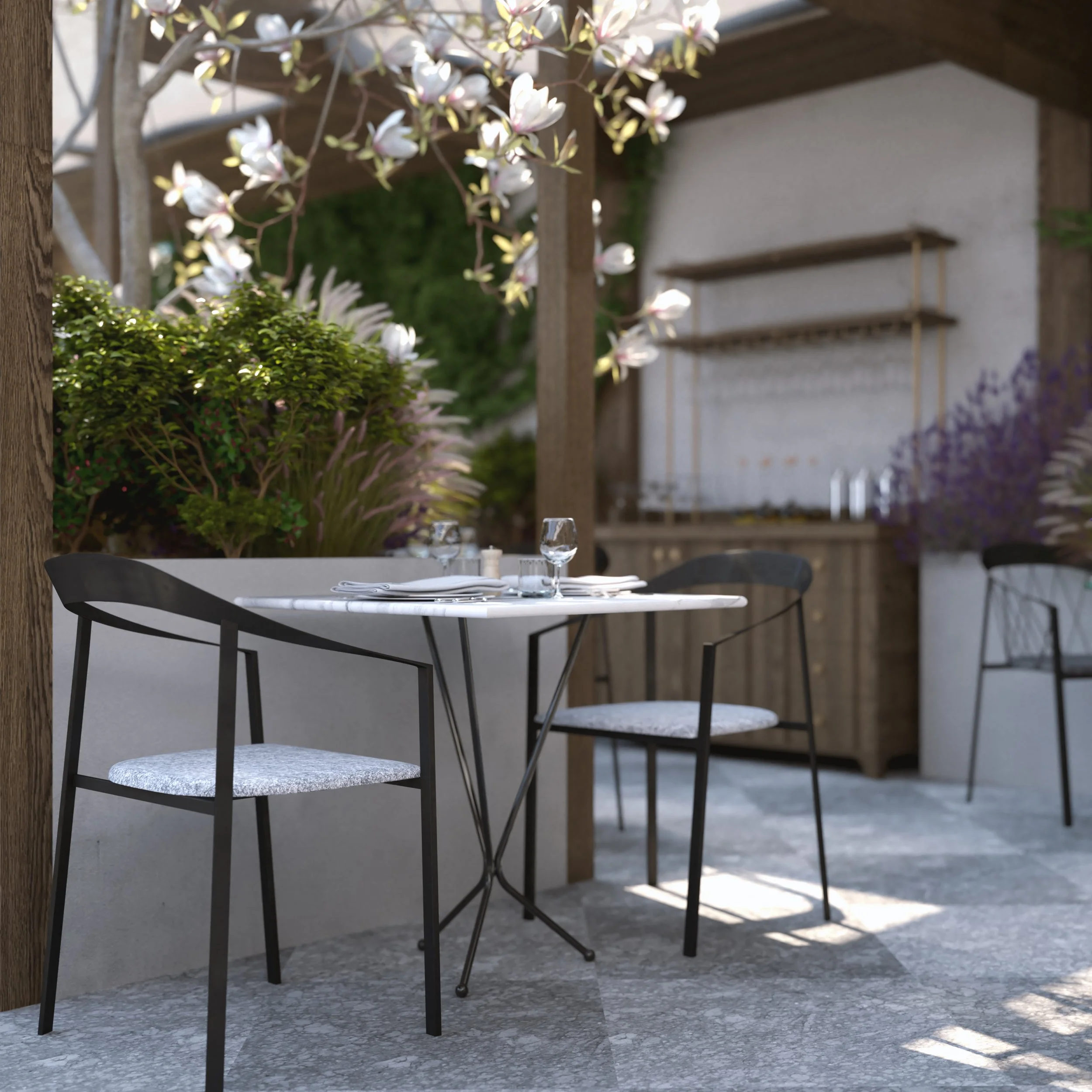 An outdoor dining scene with a small round table set with glasses, plates, and napkins, surrounded by black chairs with light gray cushions, and decorated with blooming white and purple flowers, on a patio with a stone floor.
