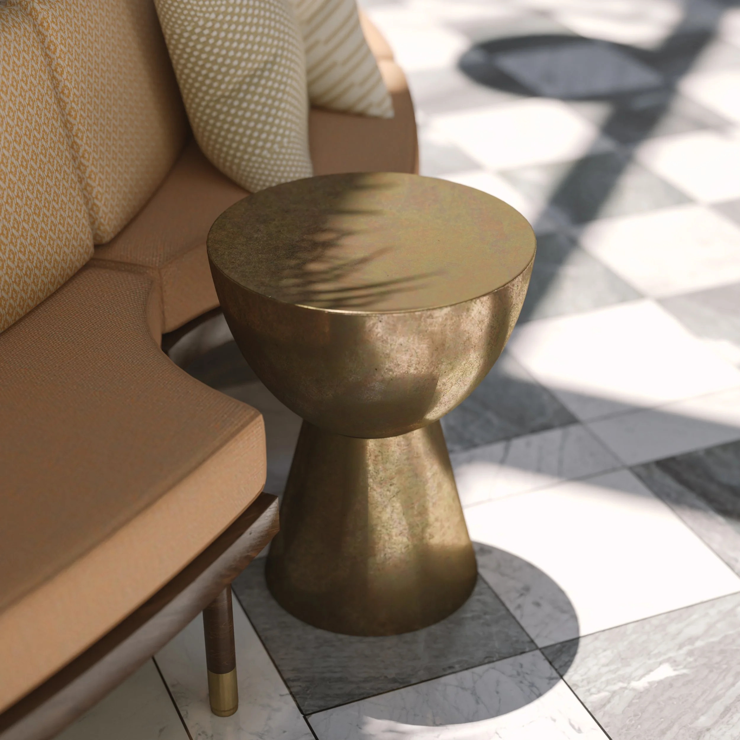 A gold-colored round side table next to a beige sofa with patterned cushions, located on a black and white checkered tile floor near sunlight and shadows.
