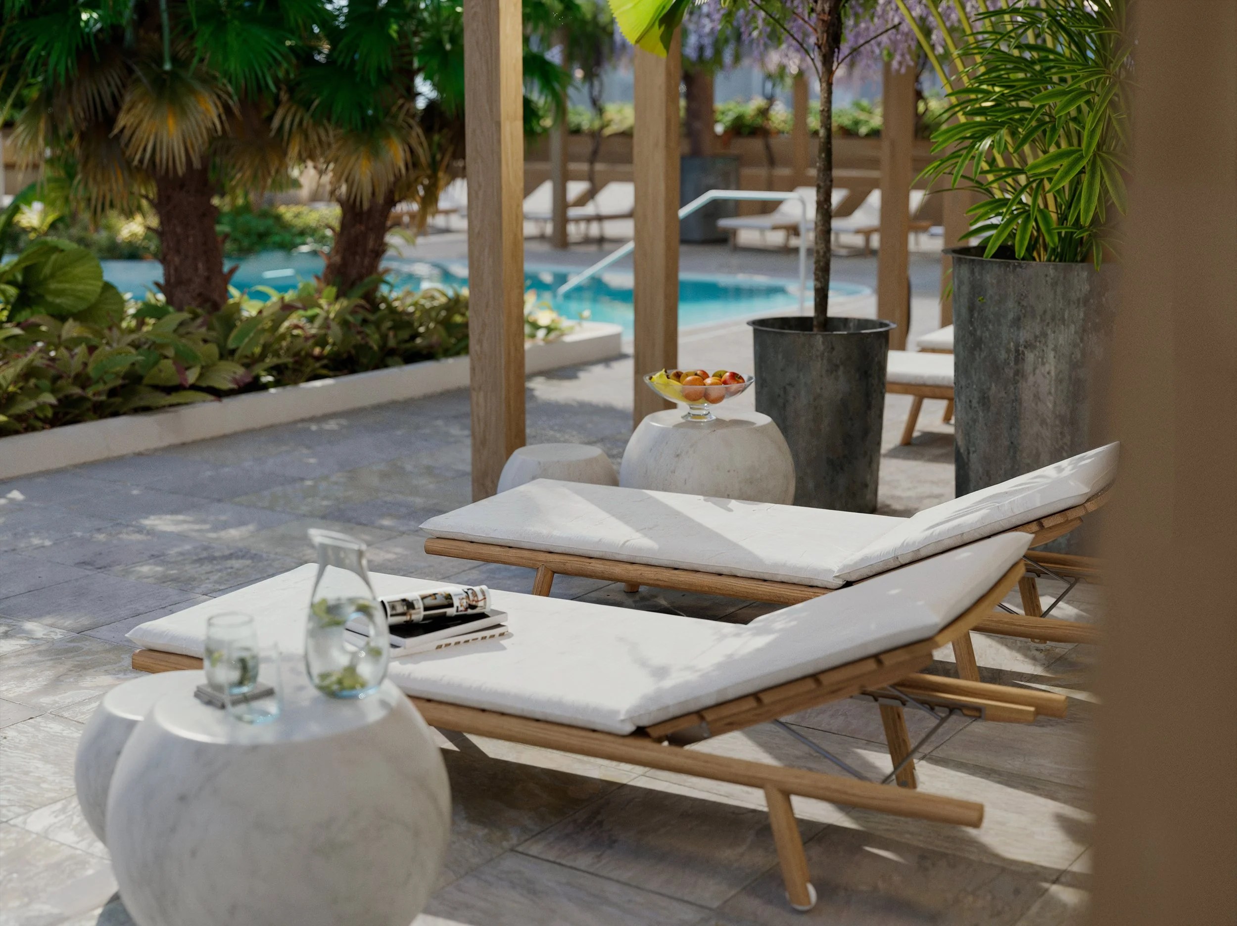 Resort poolside lounge area with two white cushioned lounge chairs, potted plants, a small marble table with a pitcher and glasses, and a background view of a swimming pool surrounded by trees and wooden structures.