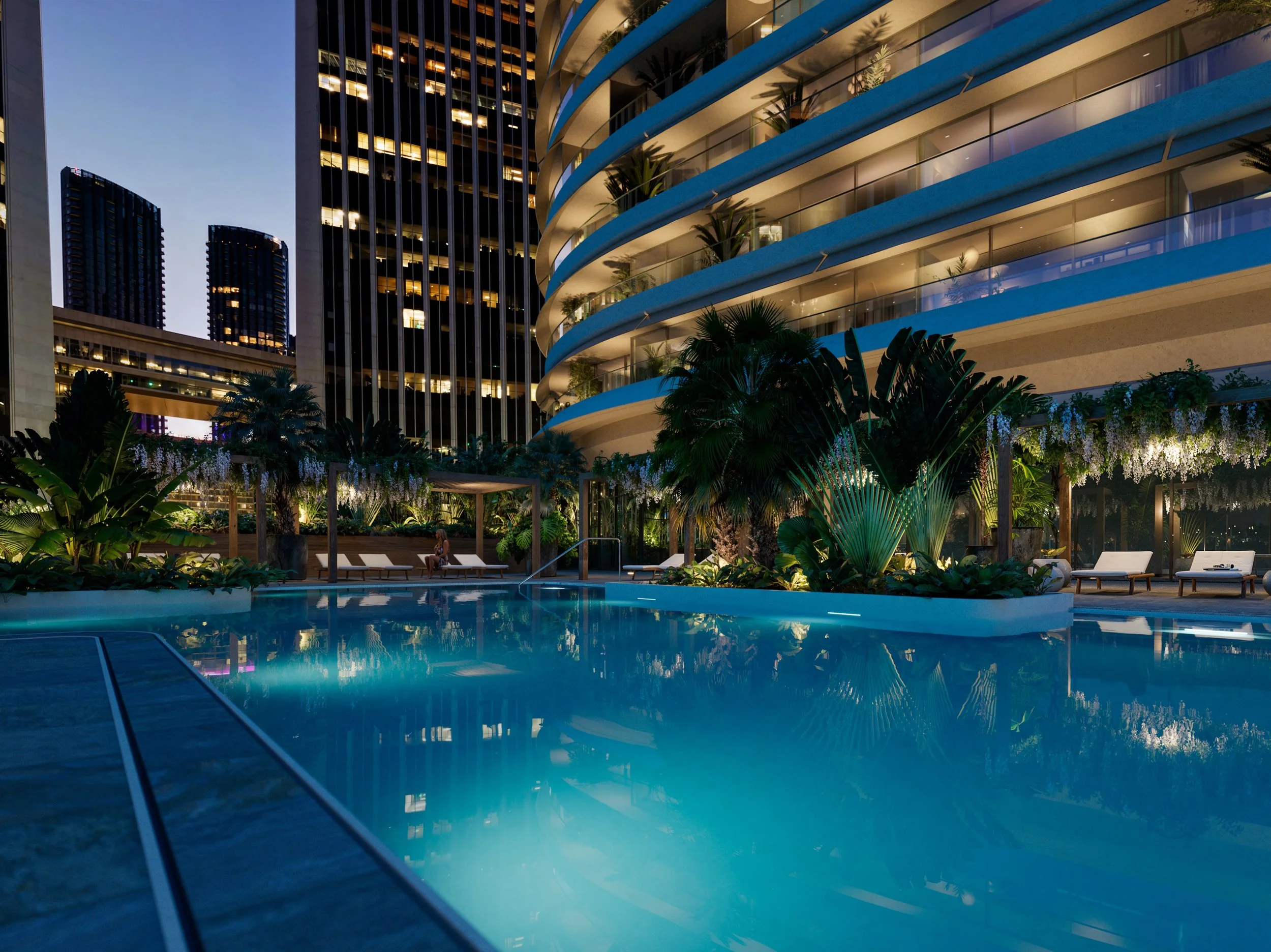 Night view of an outdoor swimming pool at a modern hotel, with tall skyscrapers in the background, lush tropical plants, and lounge chairs along the poolside.