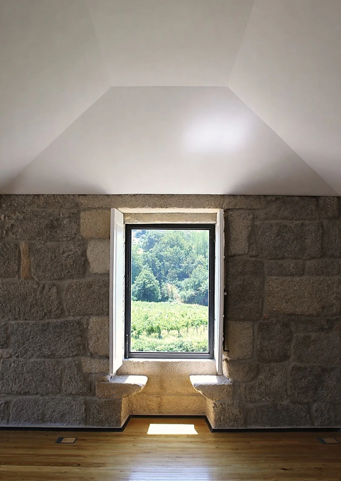 Janela conversadeira em parede de granito numa reabilitação de casa rural, enquadrando a paisagem natural exterior