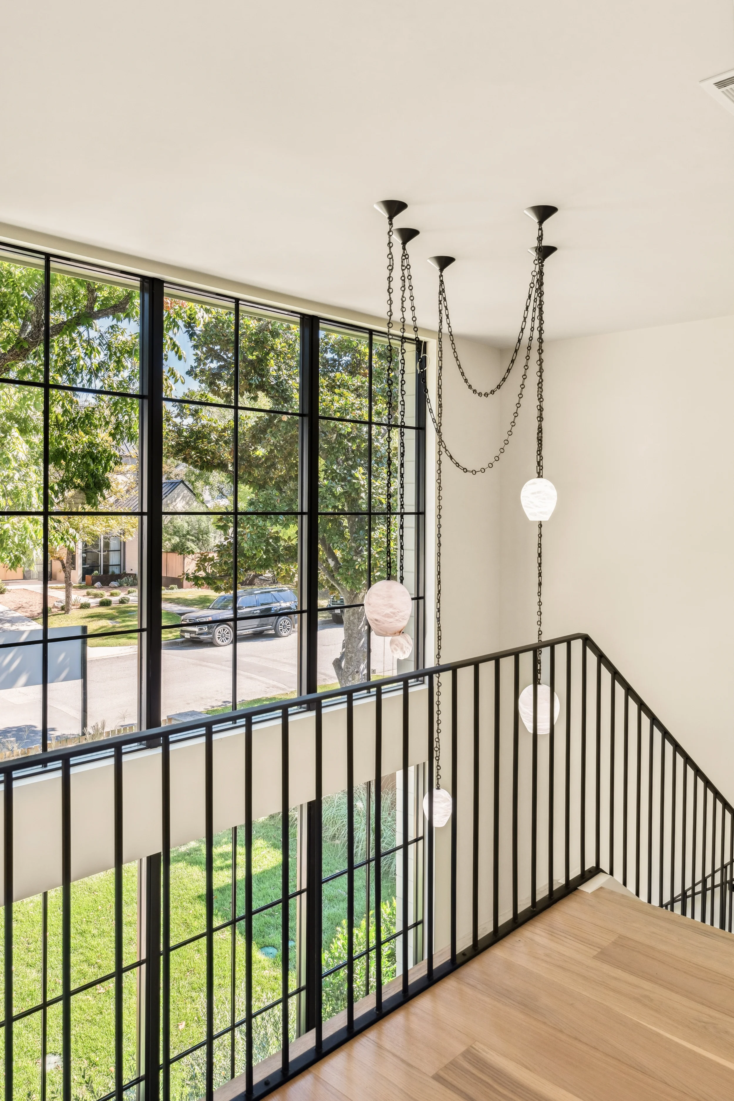 Modern staircase with black metal railing and four hanging globe pendant lights in a bright home interior with large window and view of a suburban street.