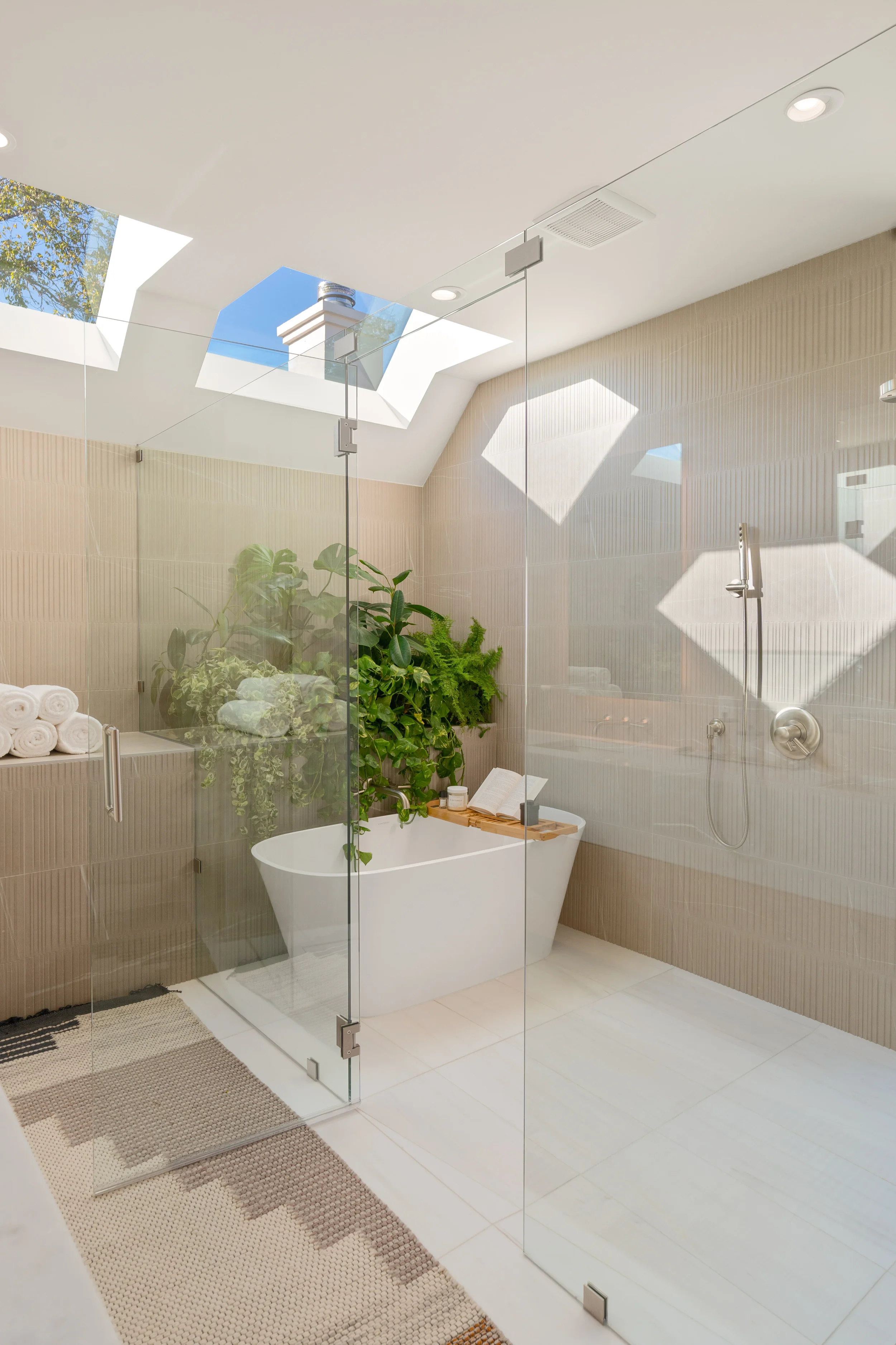 Modern bathroom with a freestanding bathtub next to green plants, a walk-in shower, and skylights letting in natural light.