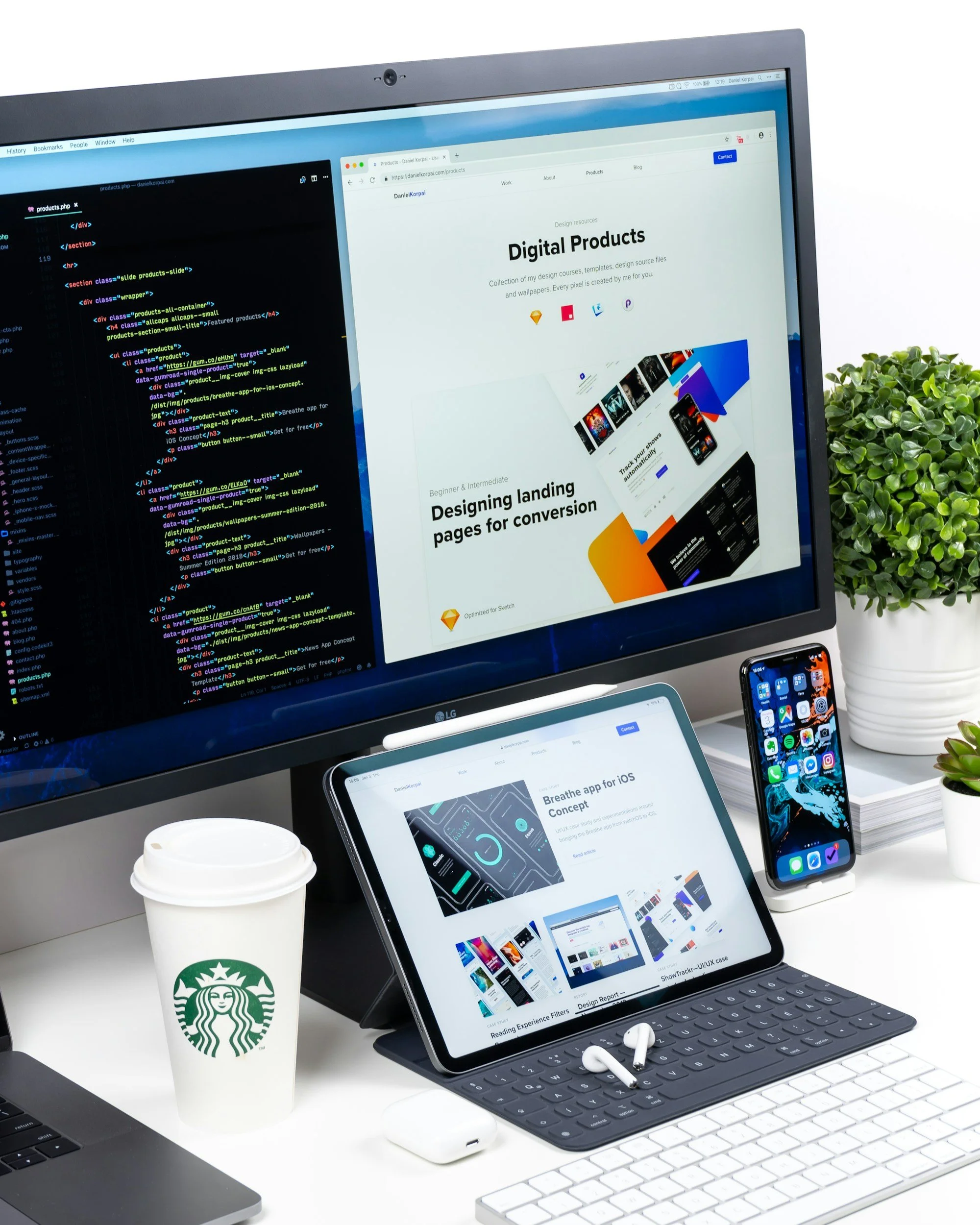 Computerbureau met monitor, tablet, smartphone, schrift en logo van Starbucks, planten, en notitieboekje.