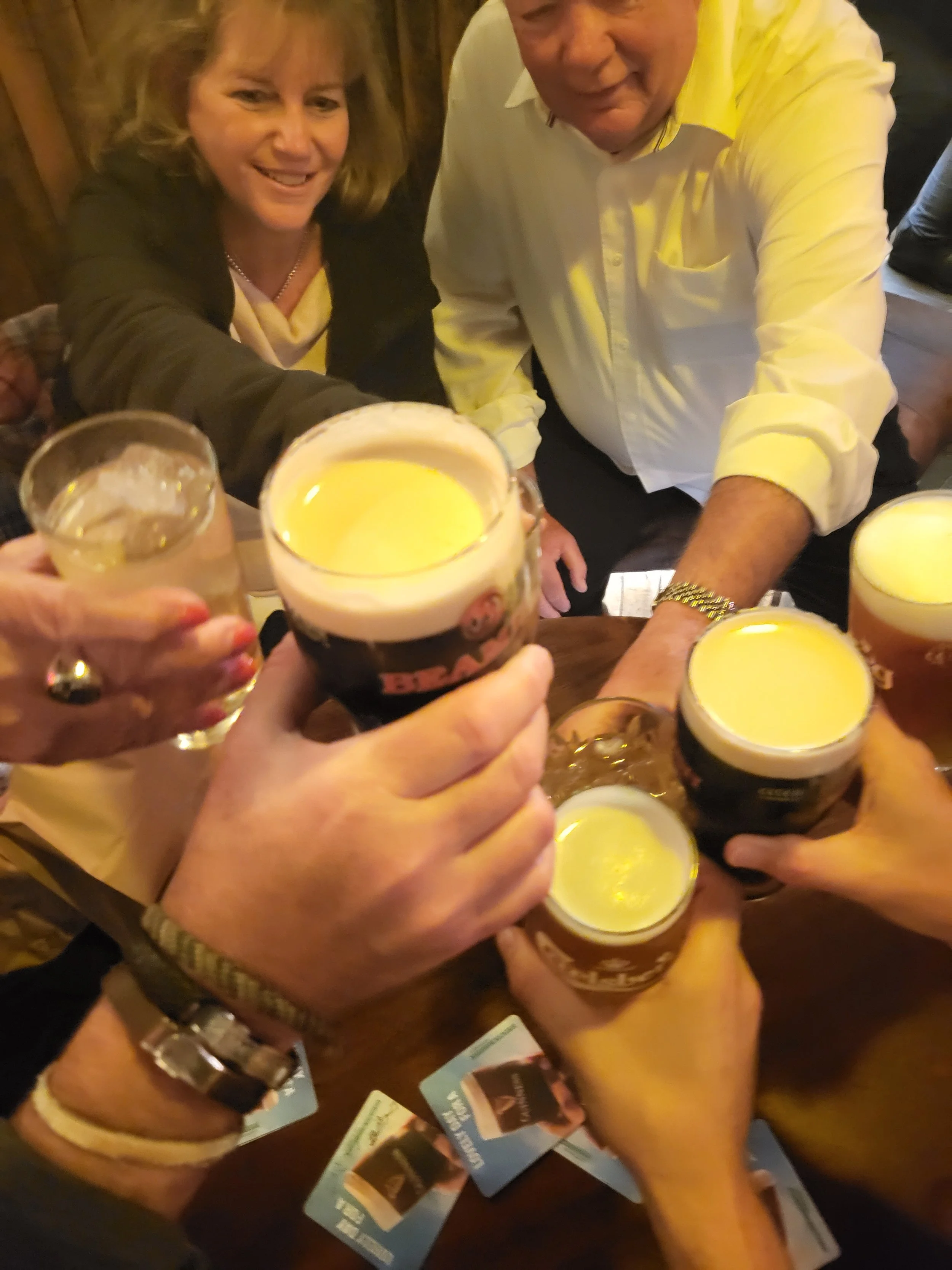 Group of people raising glasses of beer in a toast at a social gathering.