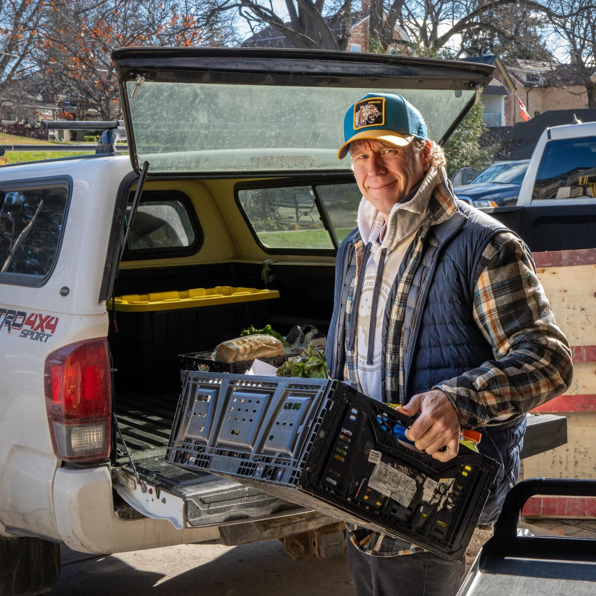 Man loading vegetables and takeaway containers into the back of a pickup truck.