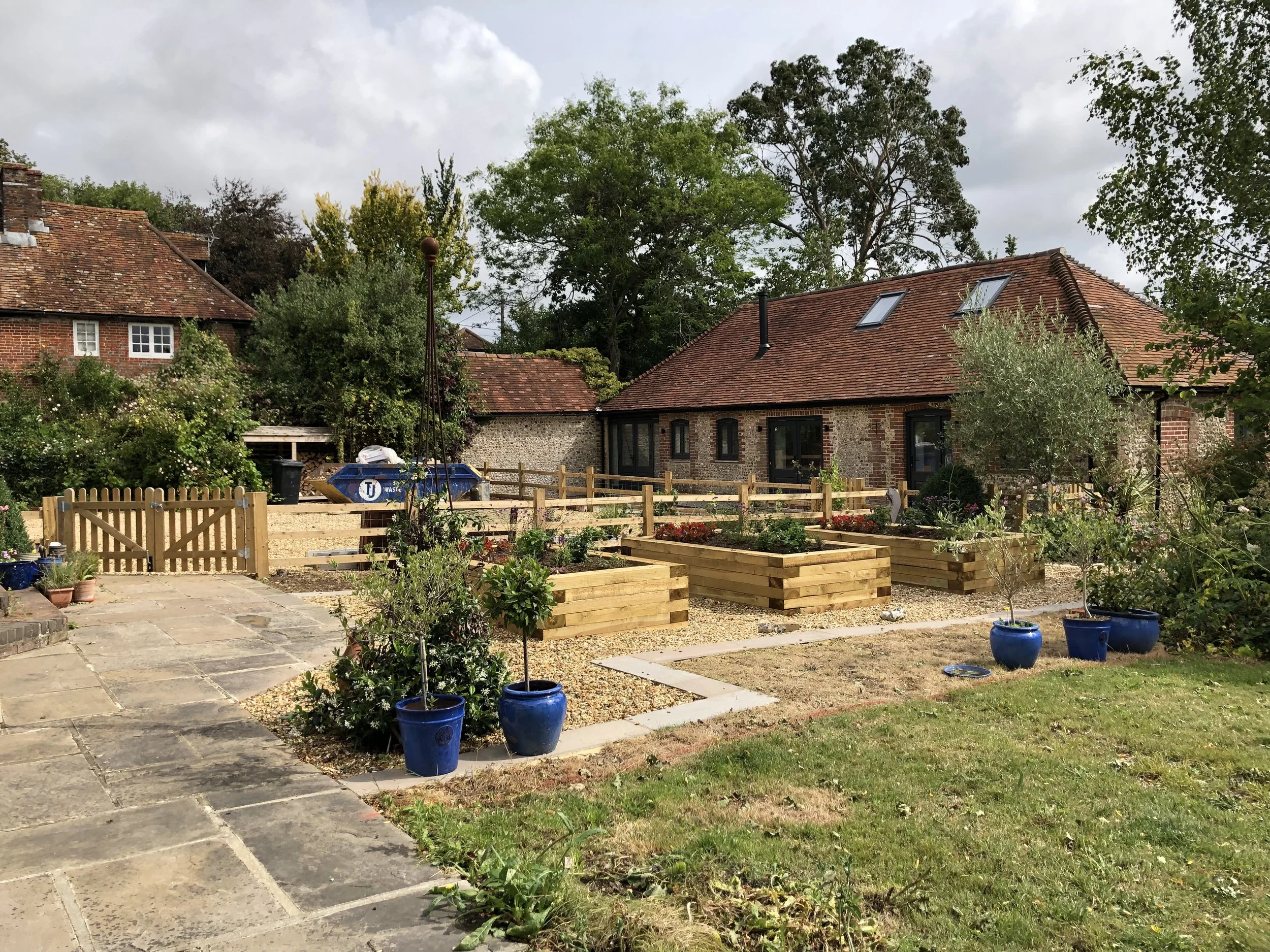 Exterior of a completed barn conversion in Chichester with landscaped garden, raised beds and timber fencing.