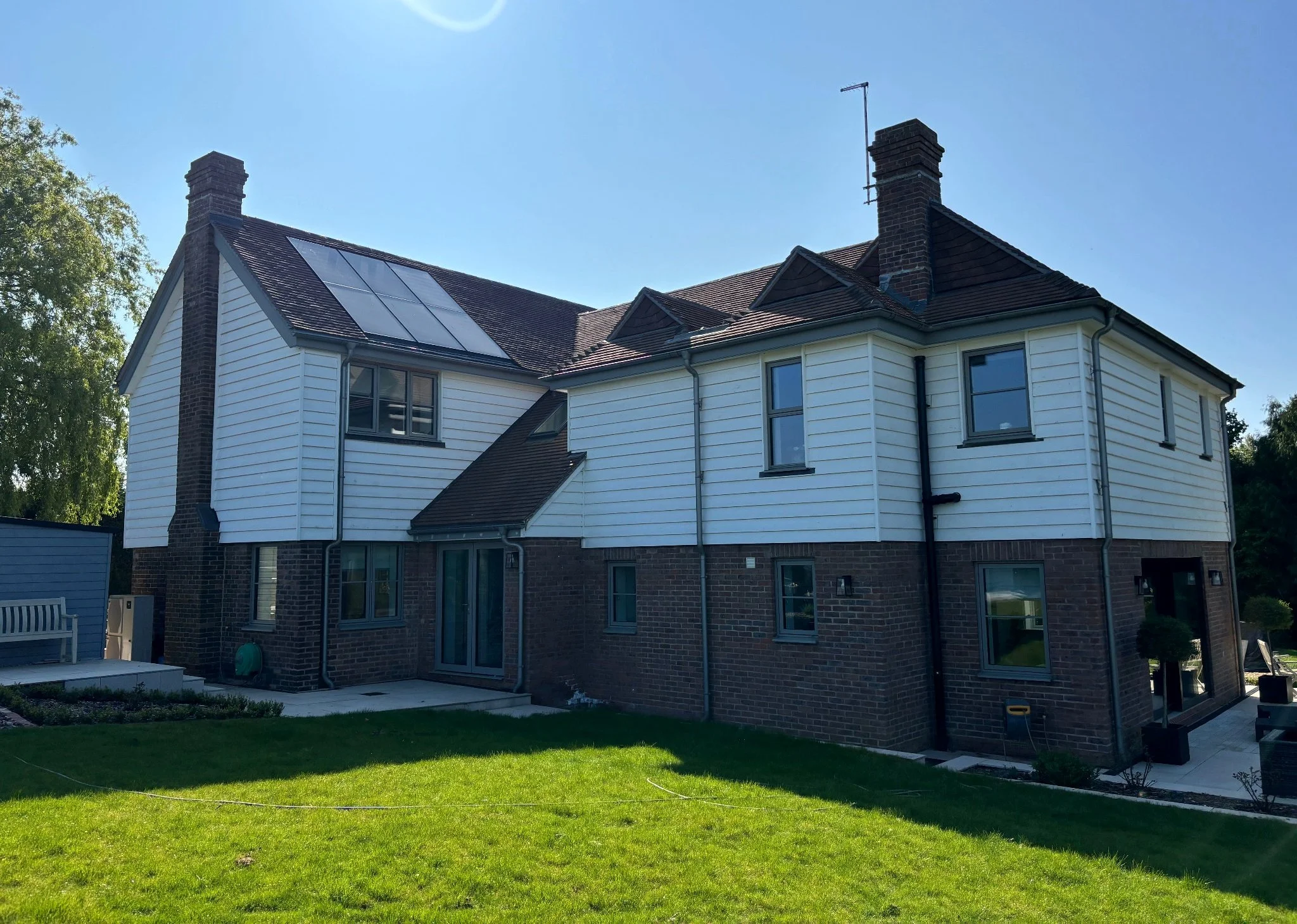Rear and side view of completed Barcombe new build, showing cladding, brickwork and pitched roof with solar panels.