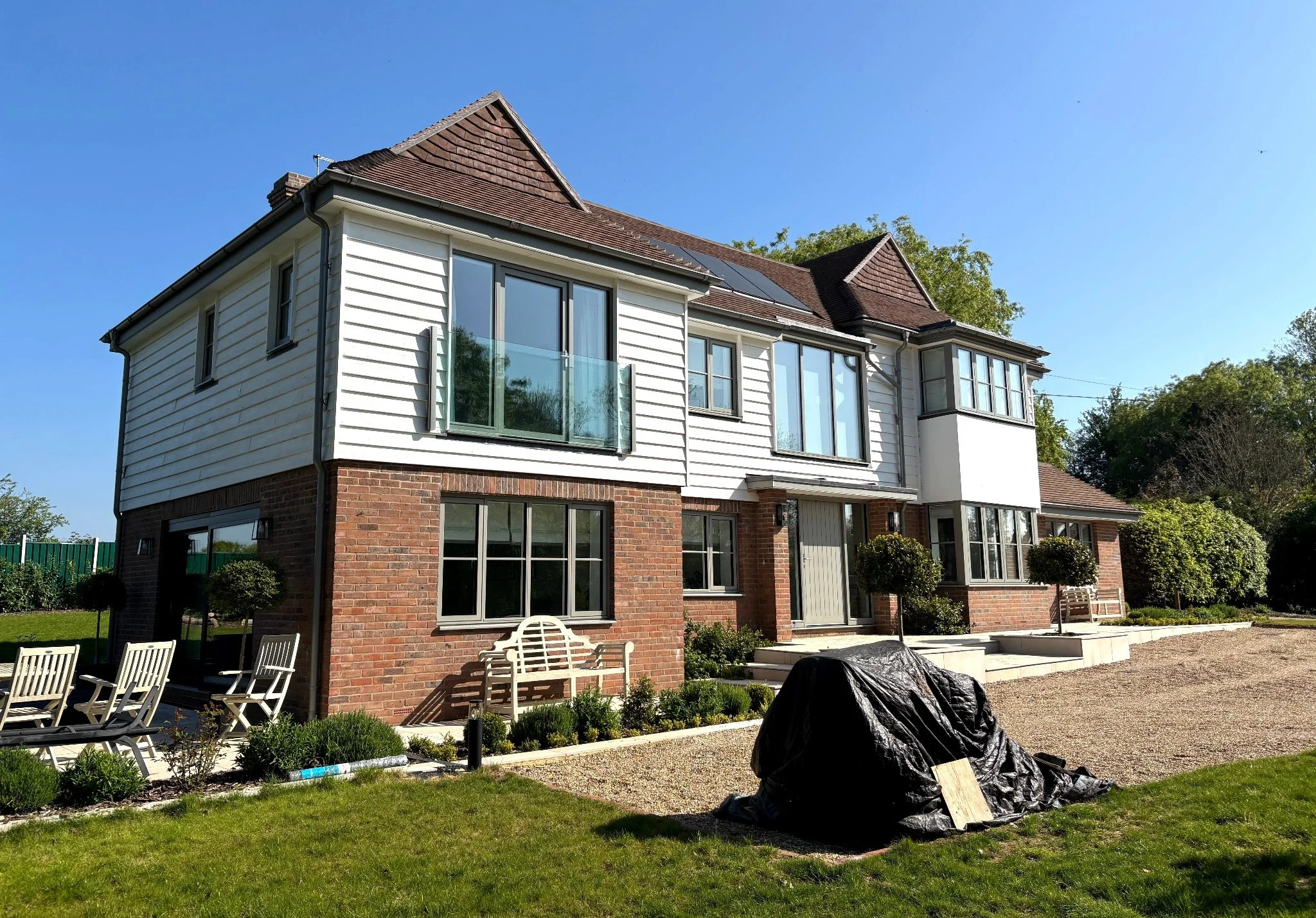 Completed two-storey new build home in Barcombe with white cladding, brickwork detailing and large modern windows.