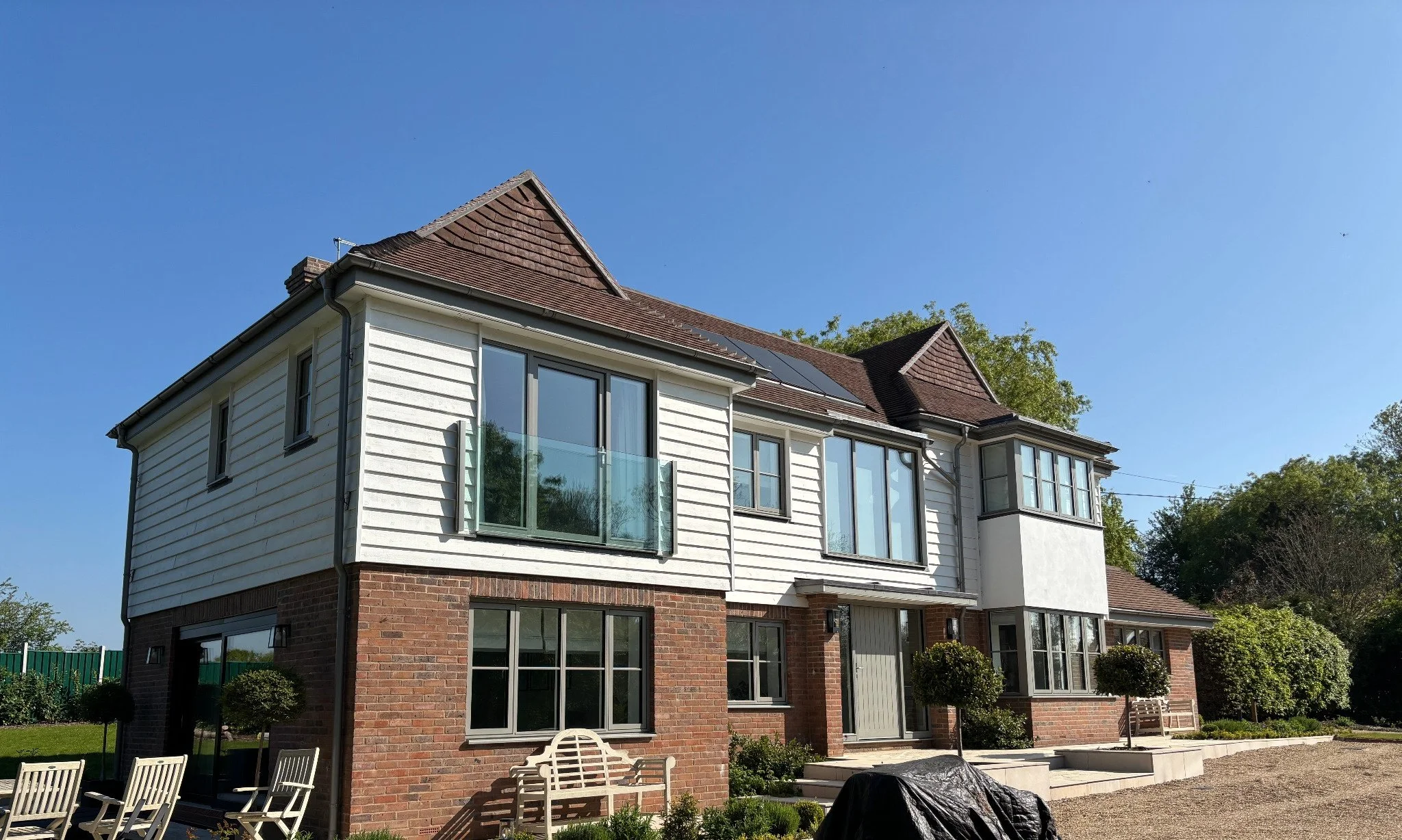 Front exterior of a completed two-storey home in Barcombe on a clear sunny day, showcasing brick and weatherboard cladding, landscaped garden and seating area.