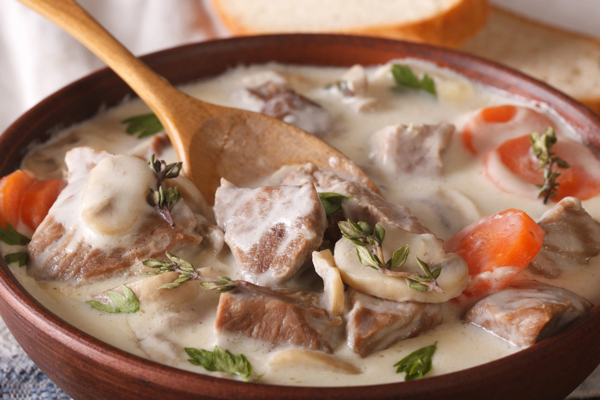 Blanquette de veau crémeuse servie dans bol rustique, morceaux de viande tendre, carottes, champignons et herbes fraîches, sauce blanche onctueuse, plat traditionnel français gourmand.