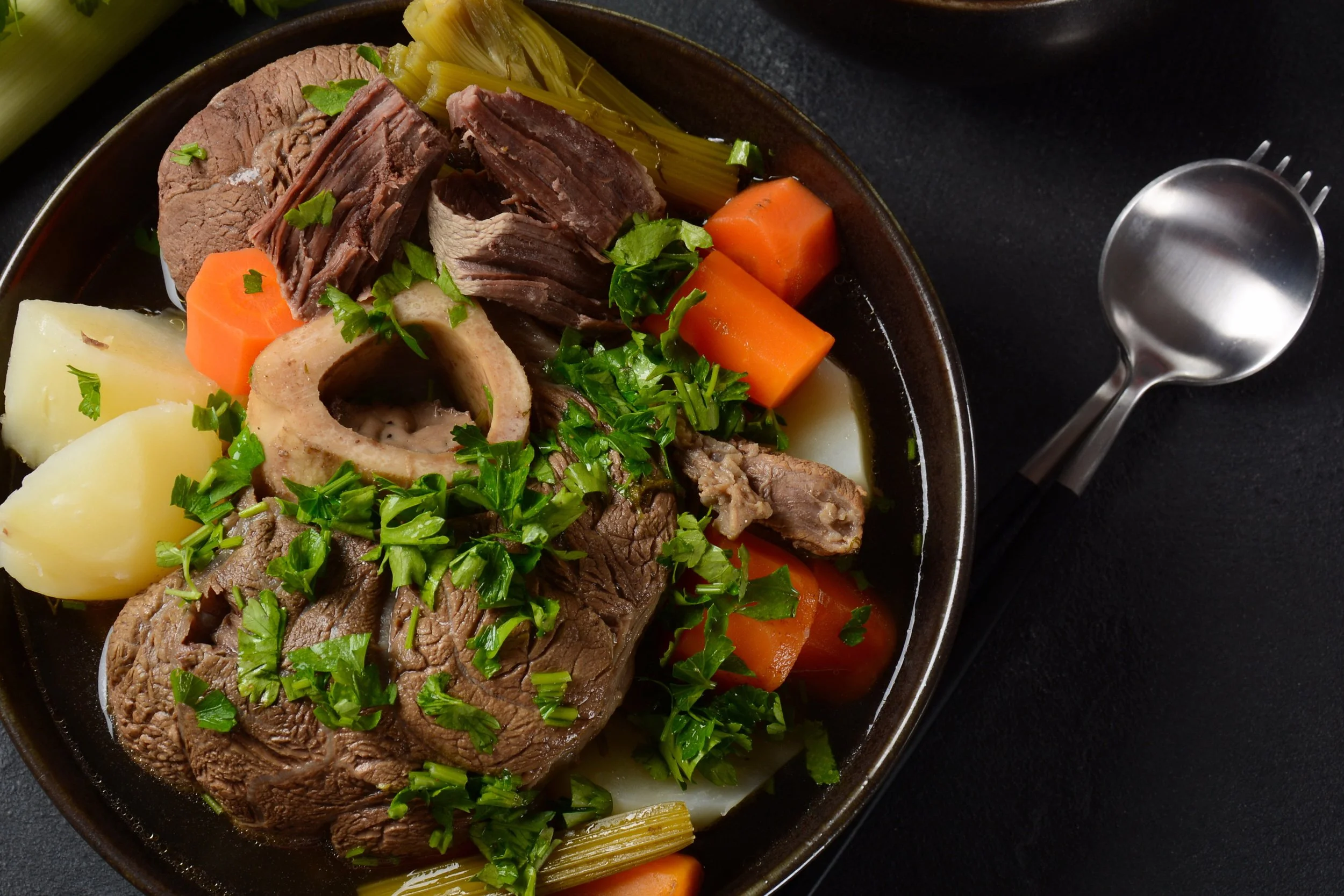 Pot-au-feu traditionnel avec morceaux de bœuf, os à moelle, carottes, pommes de terre, poireaux, garni de persil frais. Plats mijotés français.