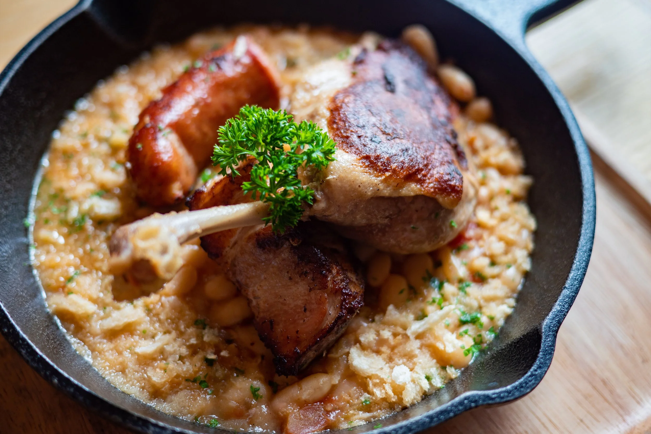 Cassoulet traditionnel servi en cocotte, haricots blancs fondants, confit de canard, saucisse et viande dorée. Plat français généreux, longuement mijoté, aux saveurs riches et authentiques de terroir