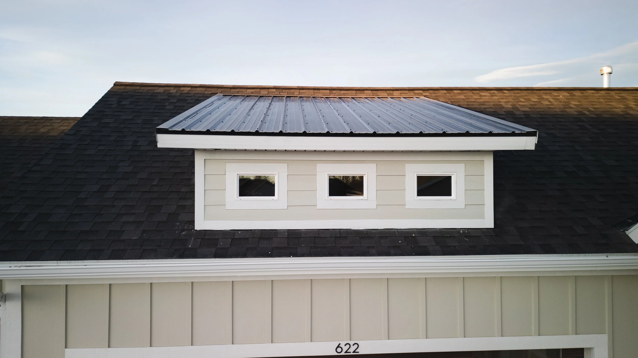 Aerial view of roof of a house with three small rectangular windows in a dormer. Real estate drone photography and videography services in Roosevelt, Vernal, Uintah Basin, Utah, and nationwide.