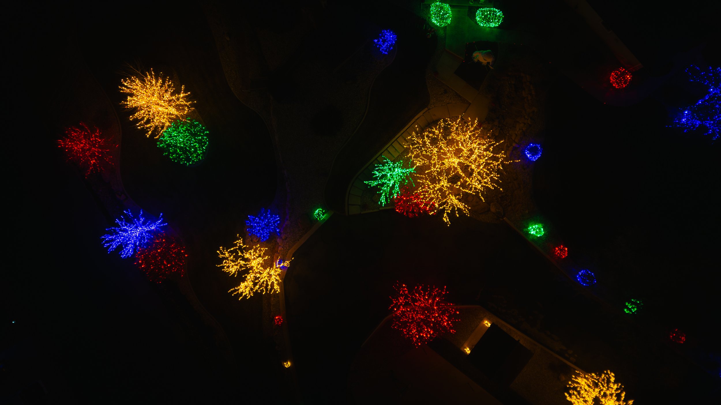 Aerial view of a park at night decorated with colorful holiday lights in the shape of trees, in red, blue, green, and yellow colors. Drone photography and videography services in Roosevelt, Vernal, Uintah Basin, Utah, and nationwide.