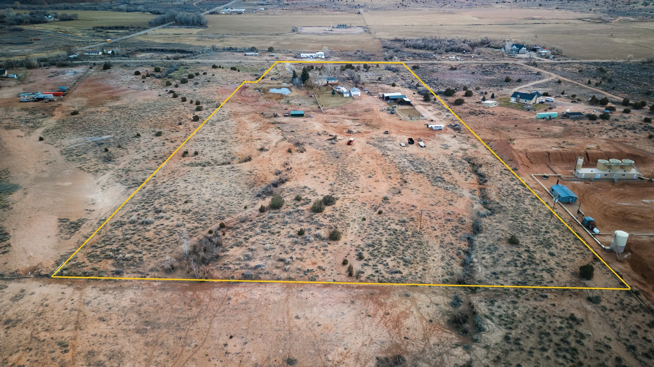 Aerial view of a large, irregularly shaped plot of land outlined in yellow, with a house, outbuildings, trees, and in a rural area with open land. Real estate drone photography and videography services in Roosevelt, Vernal, Uintah Basin, Utah.