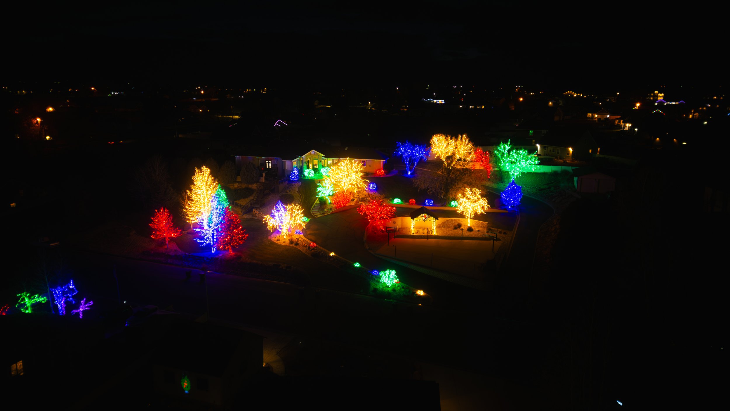 Night view of outdoor holiday light display with colorful trees illuminated in red, green, blue, and yellow lights. Drone photography and videography services in Roosevelt, Vernal, Uintah Basin, Utah, and nationwide.