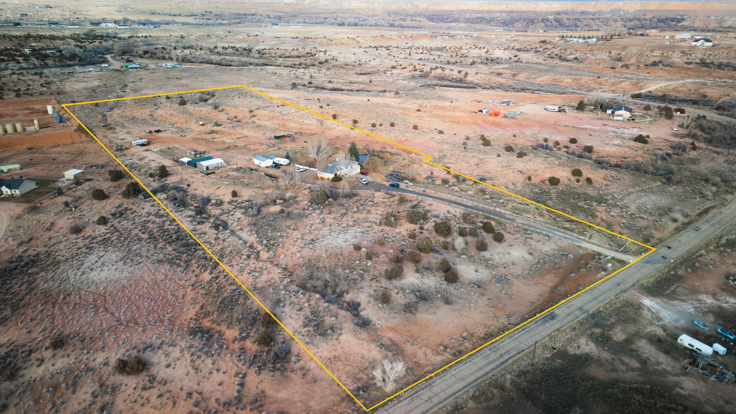 Aerial view of a large, irregularly shaped plot of land outlined in yellow, with a house, outbuildings, trees, and in a rural area with open land. Real estate drone photography and videography services in Roosevelt, Vernal, Uintah Basin, Utah.