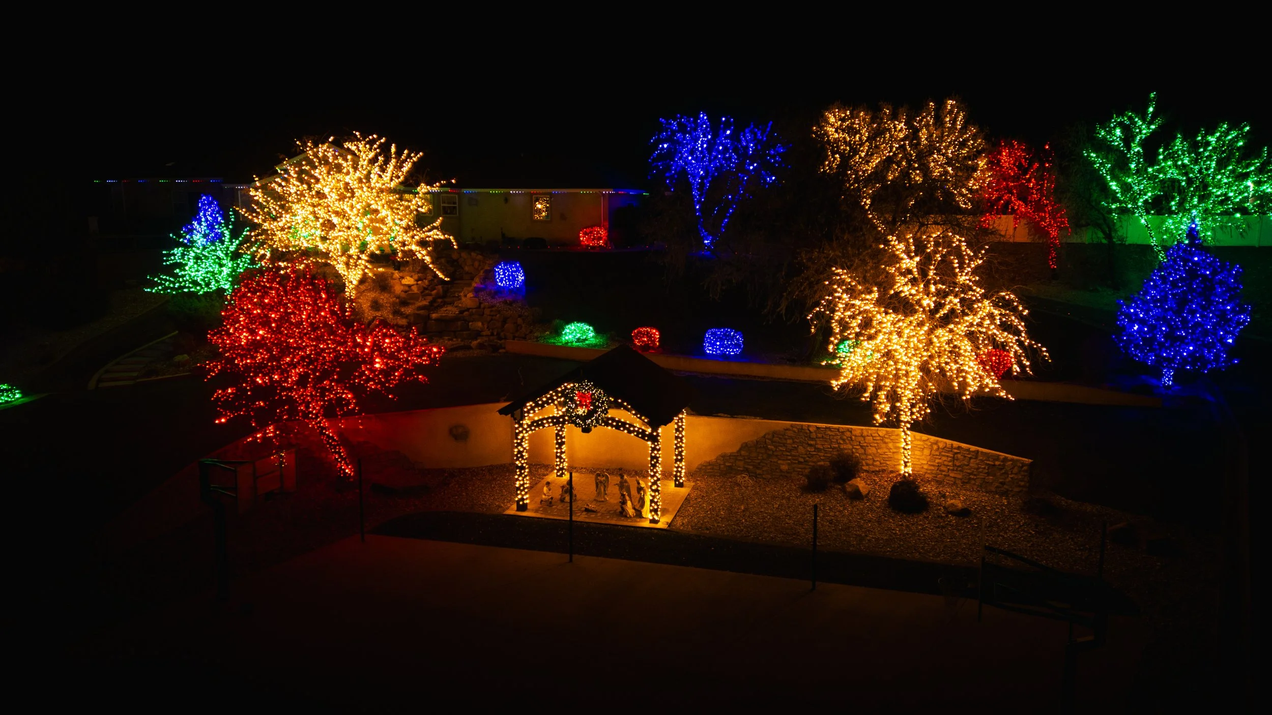 Colorful Christmas lights decorating trees and a nativity scene at night. Drone photography and videography services in Roosevelt, Vernal, Uintah Basin, Utah, and nationwide.