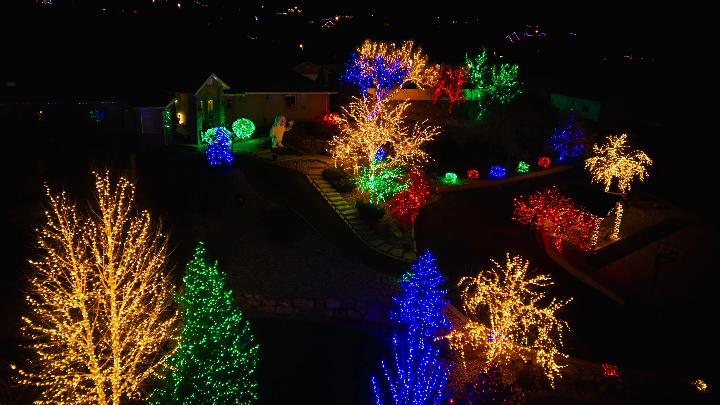 Dark night scene of a house decorated with colorful Christmas lights, including trees, bushes, and other decorations illuminated in blue, green, yellow, and red lights. Drone photography and videography services in Roosevelt, Vernal, Uintah Basin, Ut