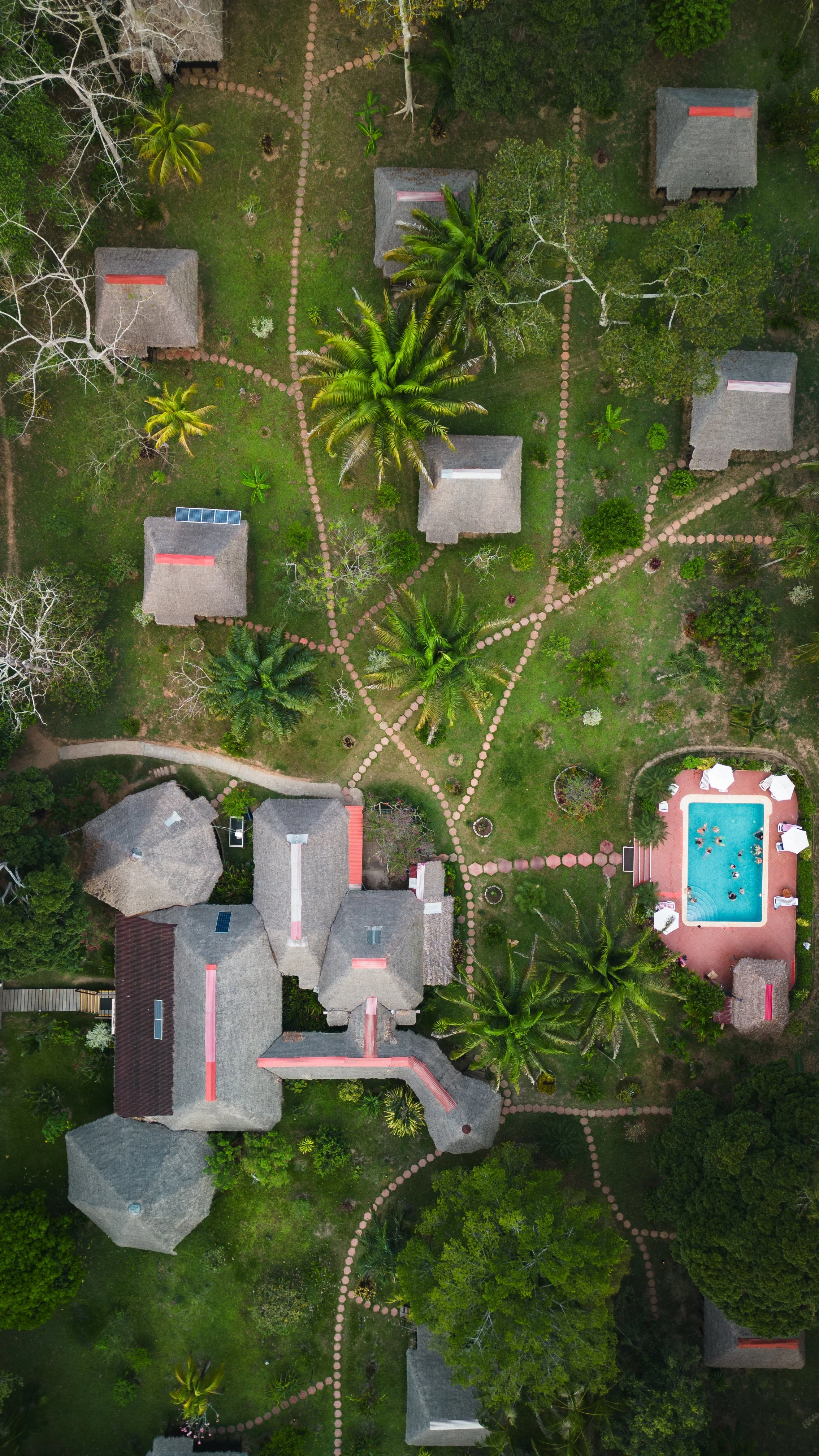 An aerial view of a resort with multiple buildings, a swimming pool, palm trees, and winding paved pathways.