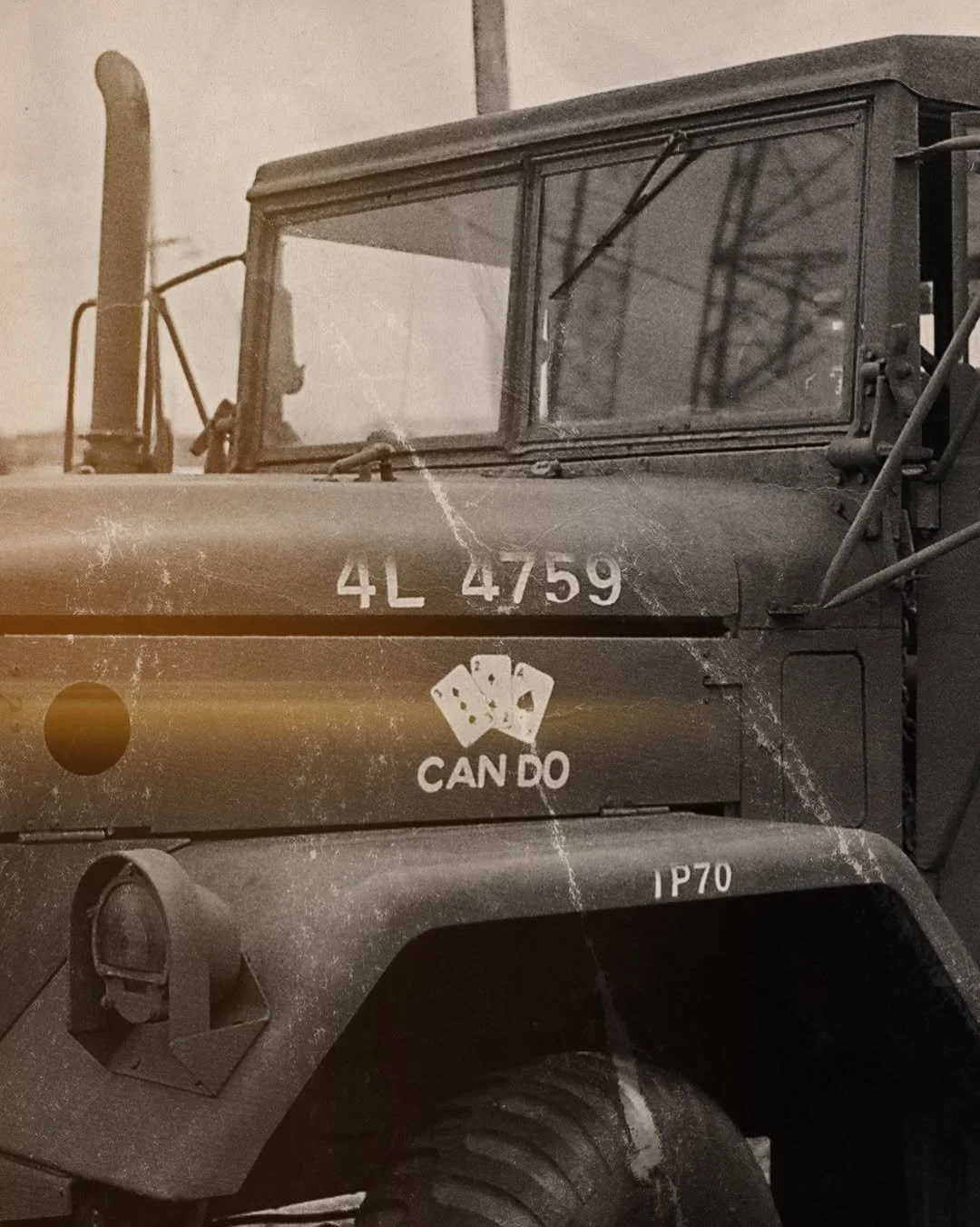 Close-up of a vintage military vehicle, likely a jeep, with a weathered appearance. The vehicle has the number "4L 4759" painted on the hood, and a decal of playing cards with the words "CAN DO." The vehicle features rugged tires, a windshield with a