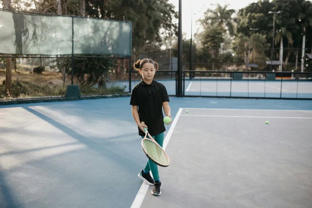 A young girl holding a tennis racket on a court with tennis balls around her