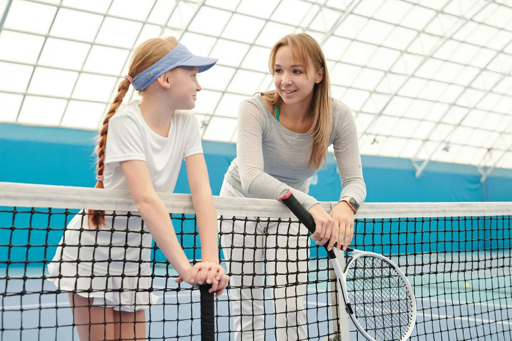 Two young women talking at the net on an indoor court