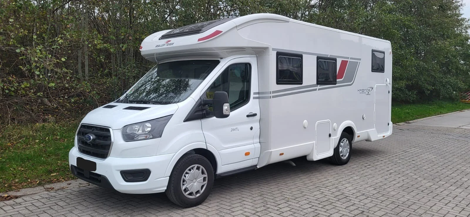 Een wit camperbus geparkeerd op een weg met een bos op de achtergrond.