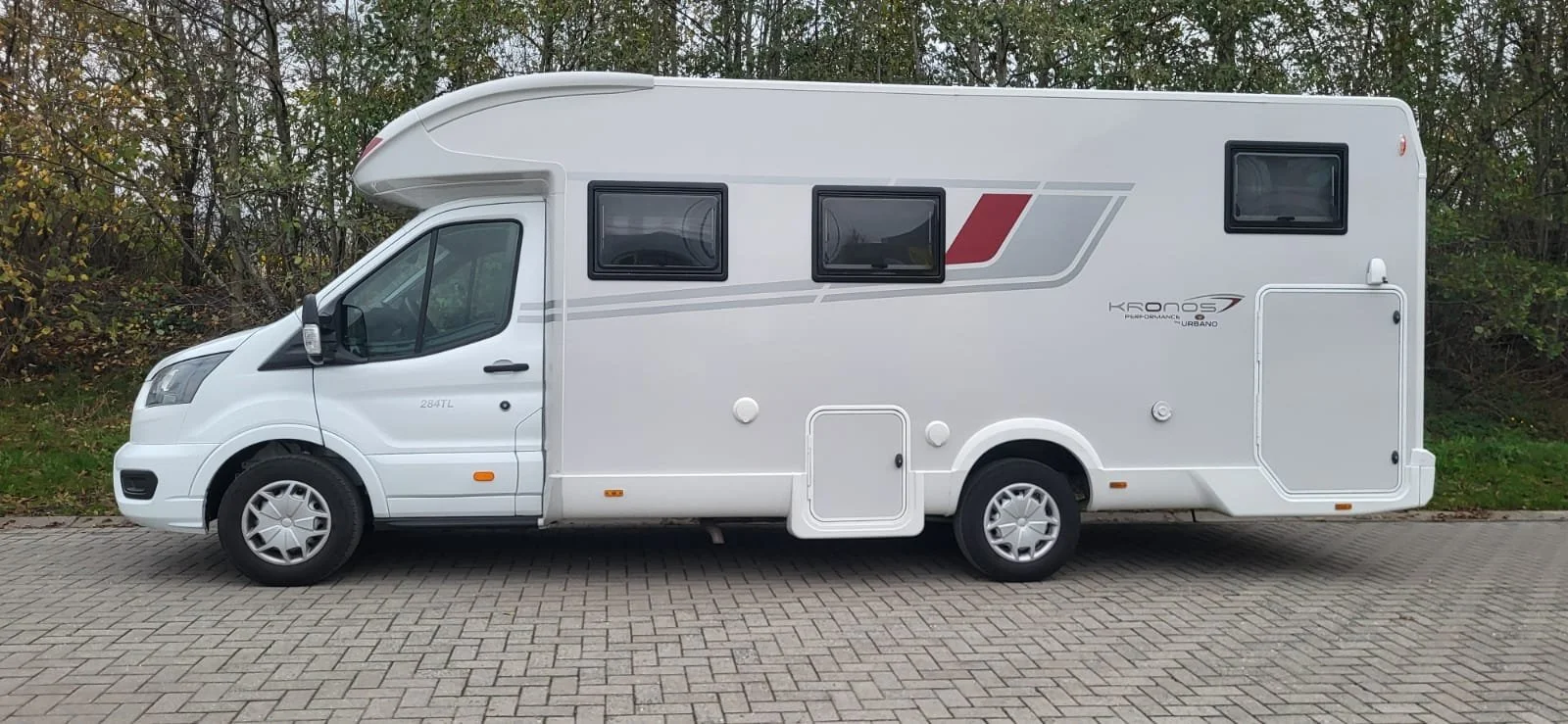 Een witte camperauto geparkeerd op een betegeld pad, met groen struikgewas op de achtergrond.