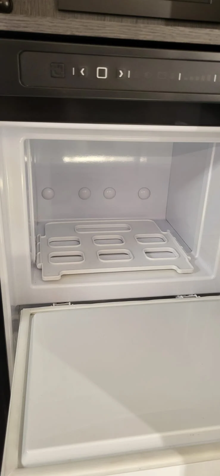 Leeg mini vrieskastje met witte binnenkant en roosters op de bodem.