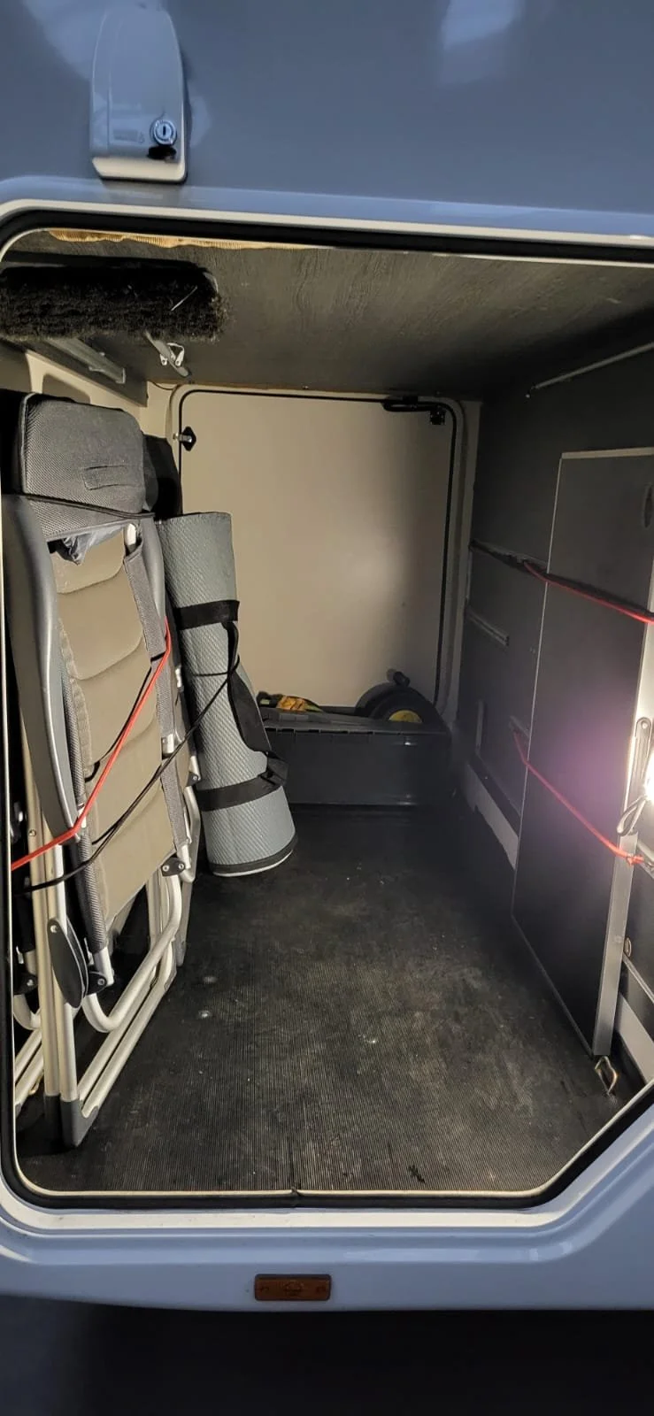 Binnenkant van een caravan of camper met campinguitrusting, zoals een stoel, matje en gereedschap.