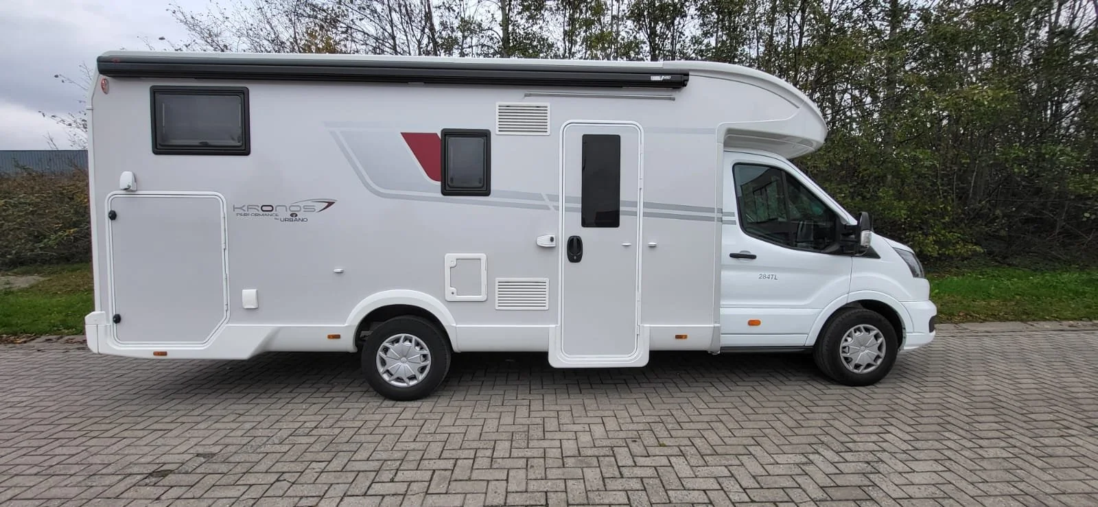 Wit kampeerbus geparkeerd op een weg met begroeiing op de achtergrond.