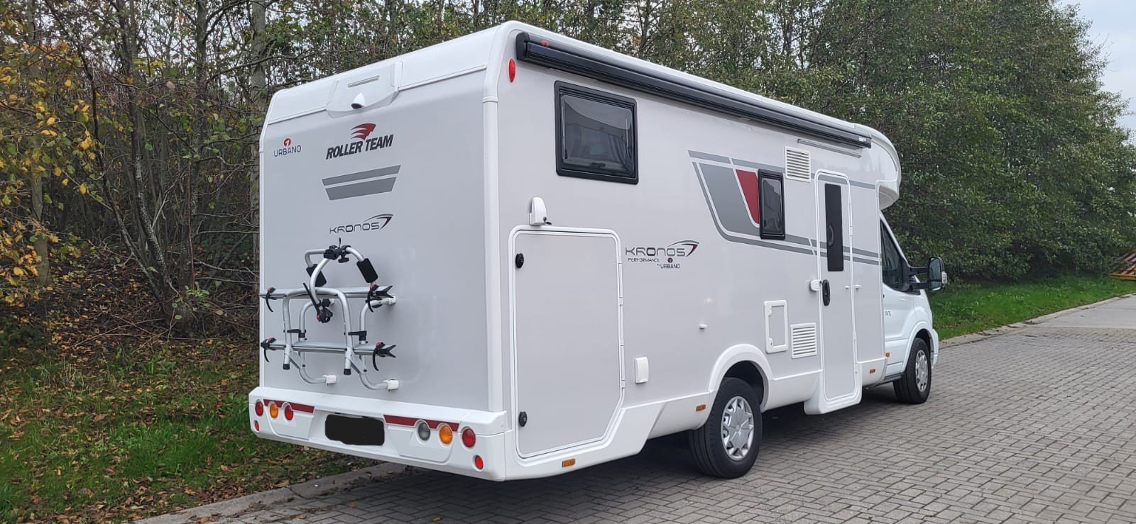 Wit camper op een parkeerplaats naast groene bomen.