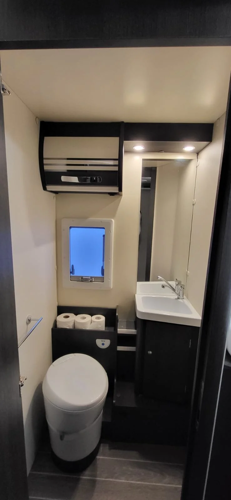 Kleine badkamer met een wc, wasbak, spiegel, kast, en een klein raam.