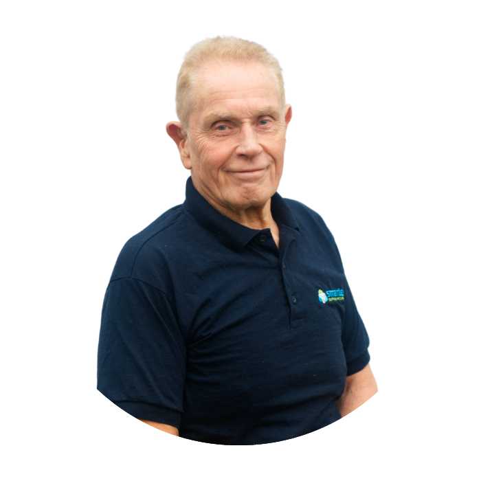 Older man with short, light-colored hair and a slight smile, wearing a navy blue polo shirt with a logo, standing against a white background.
