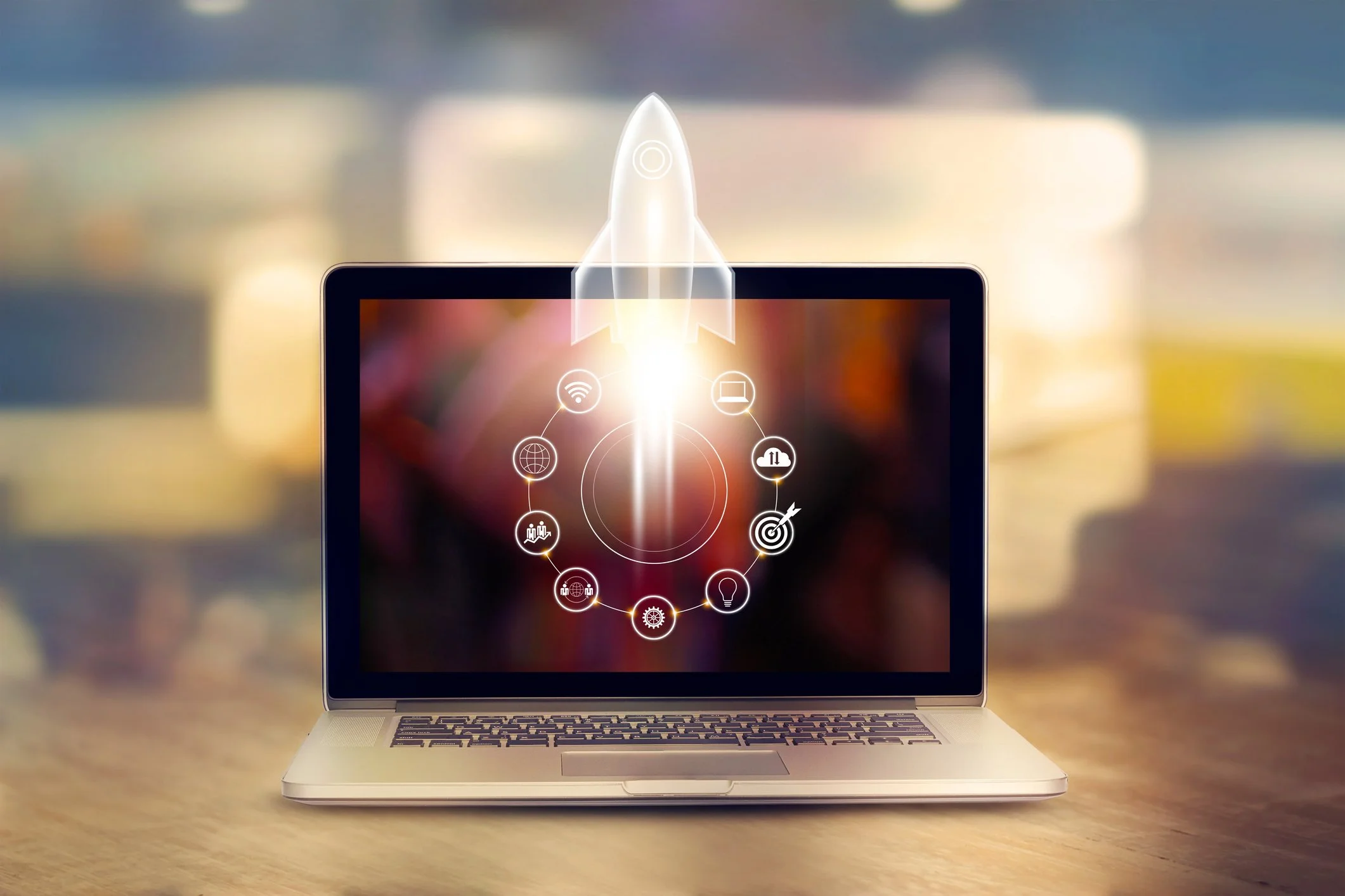 Laptop computer with a digital rocket graphic and various technology icons displayed on the screen, set on a wooden surface with a blurred background.