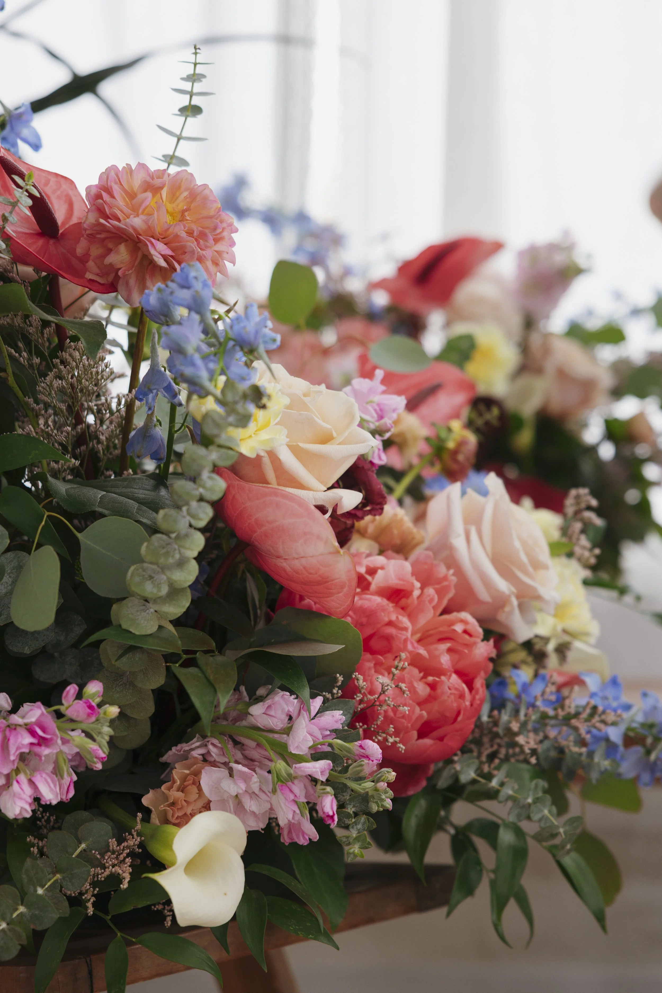 A colorful arrangement of various flowers including pink, peach, white, red, and purple blooms with green leaves.