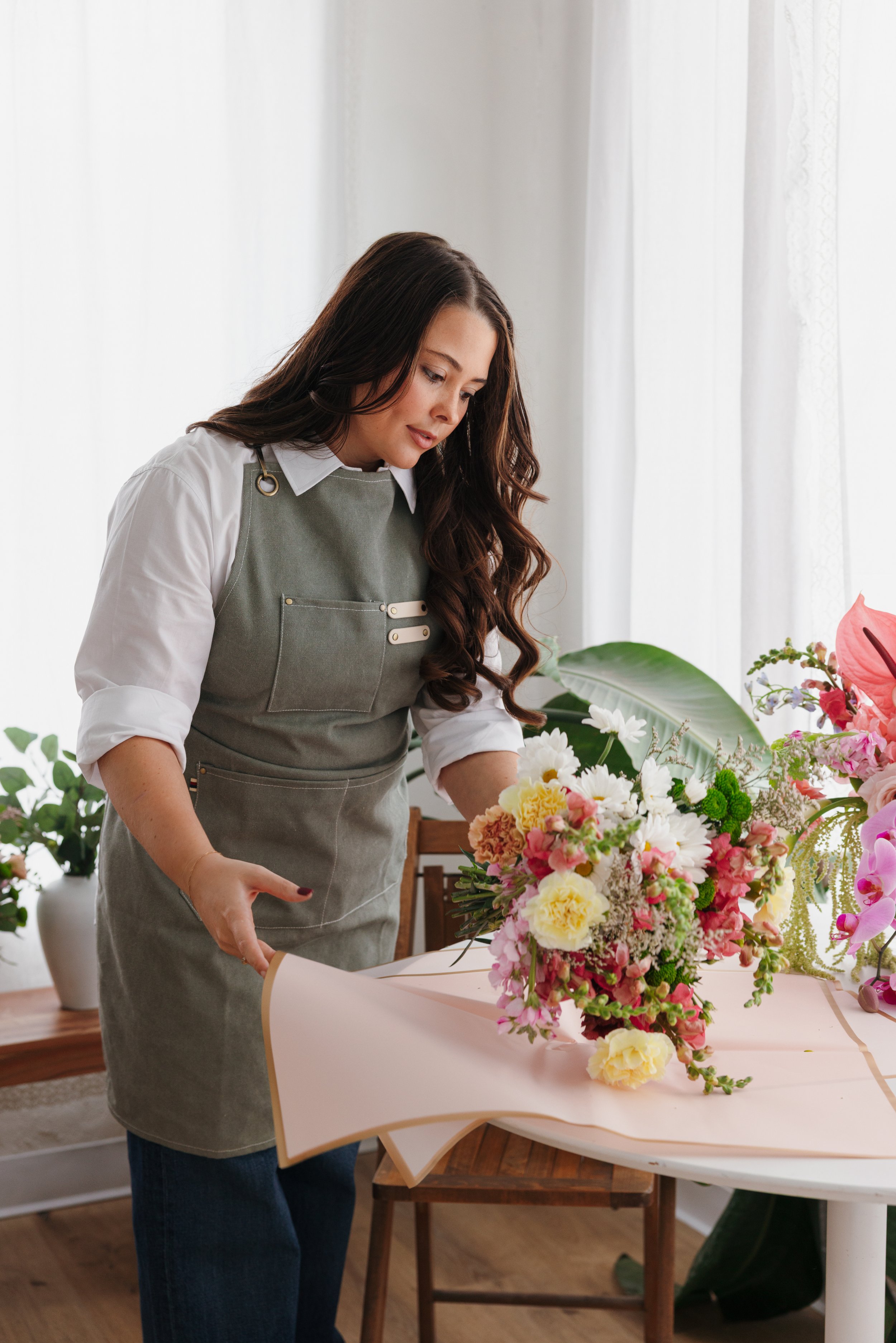 A woman arranging a bouquet of colorful flowers on a table in a bright room.