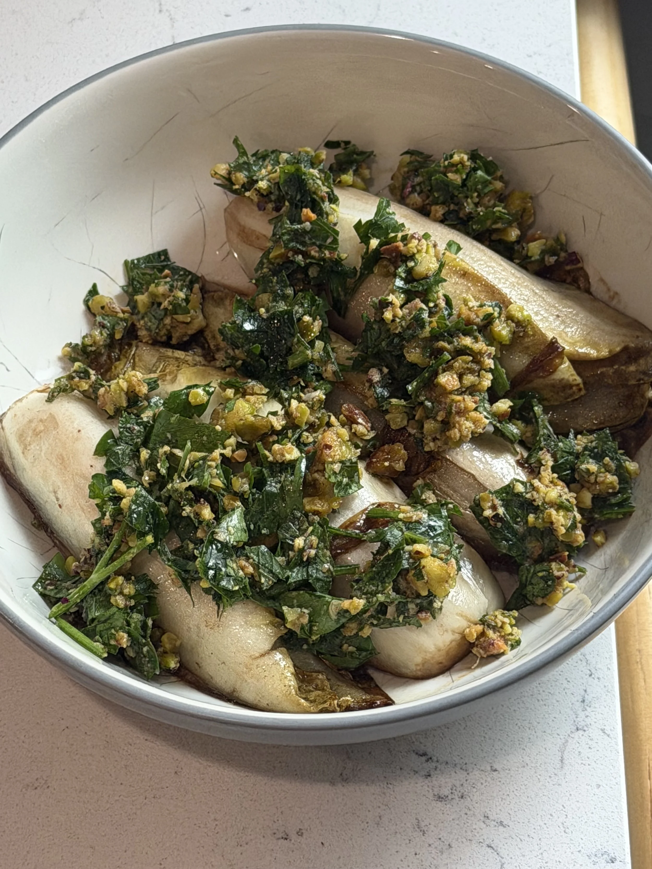 Fresh whole eggplants topped with chopped greens and yellow seasoning in a metal bowl.
